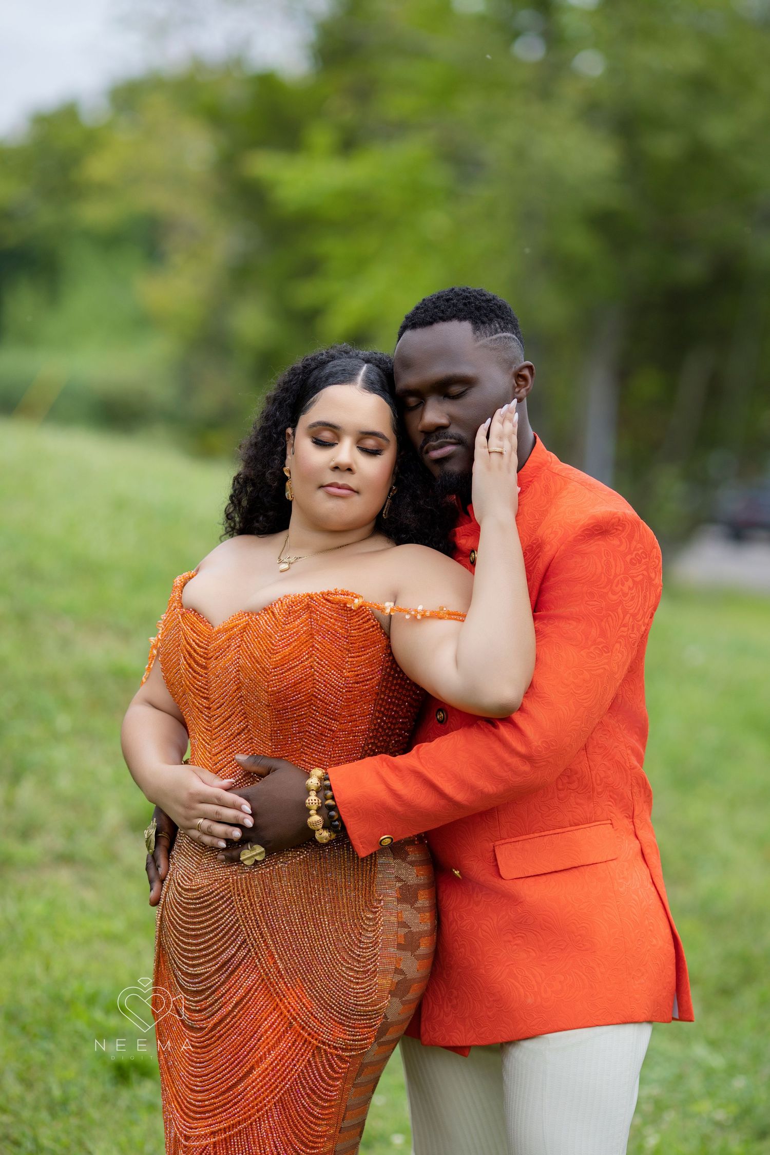 A couple embraces outdoors wearing coordinating orange formal attire.