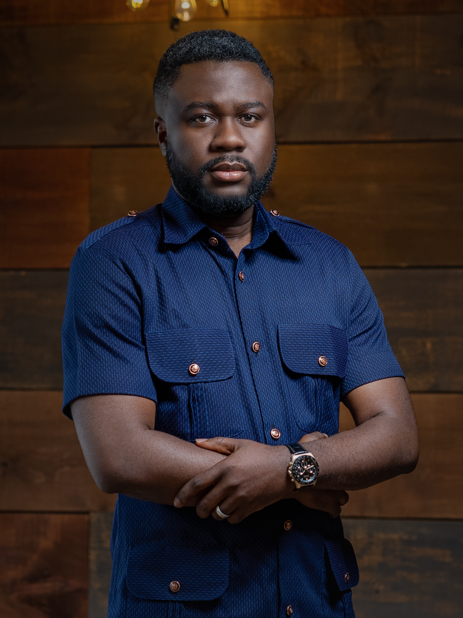 Portrait of a person in a navy blue utility shirt with copper buttons against wooden paneling.
