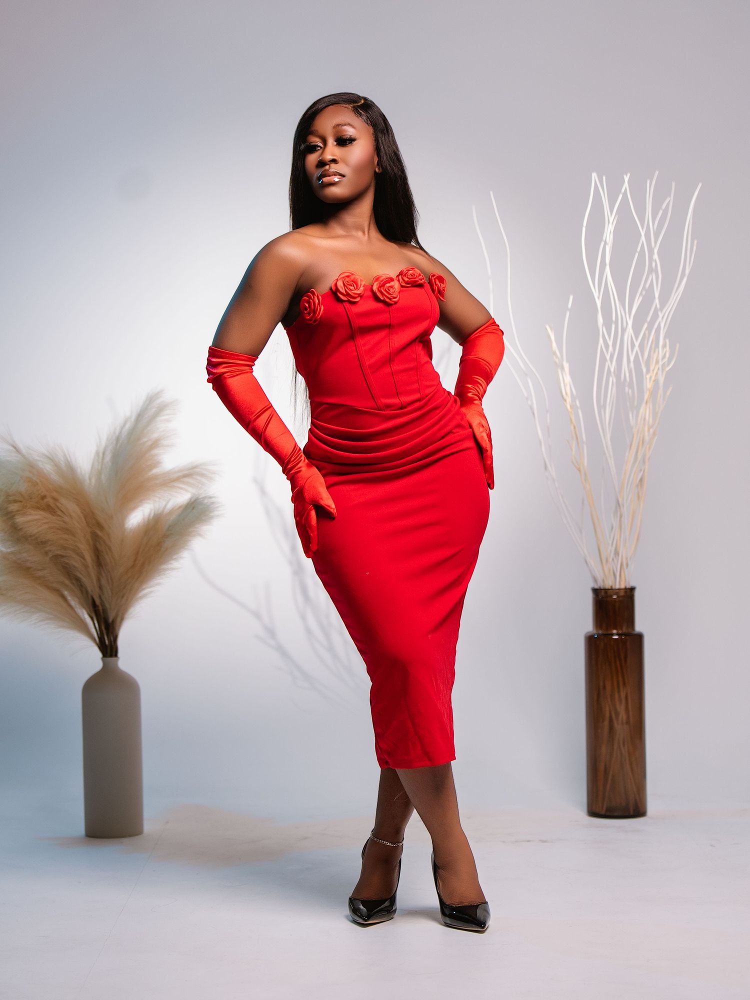 A striking fashion photograph of a red strapless cocktail dress with matching gloves against a minimalist backdrop.