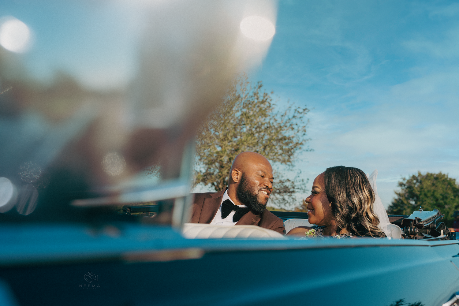 Romantic moment captured through car window with blue sky background.
