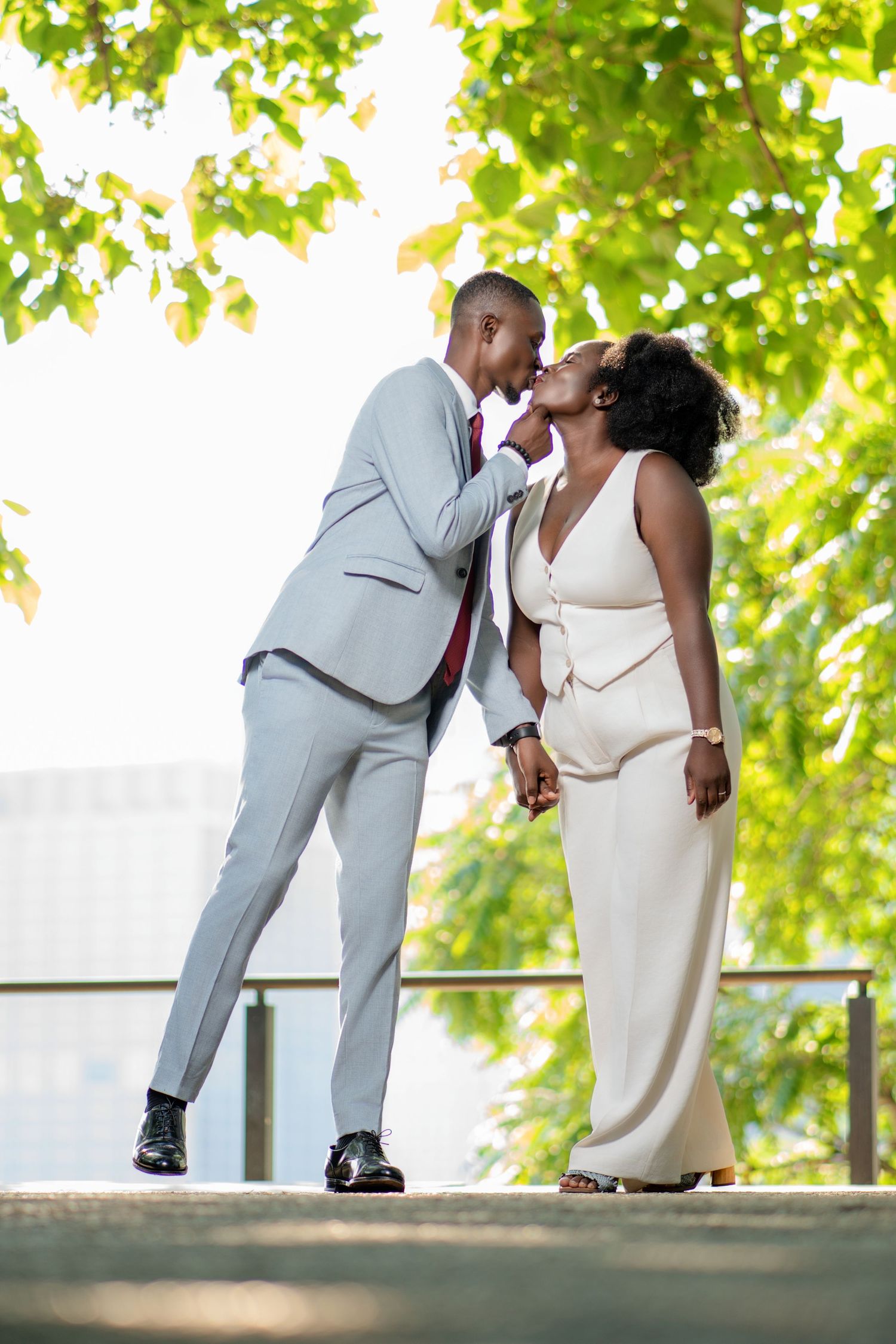 Romantic couple in formal attire sharing an intimate moment under green trees.
