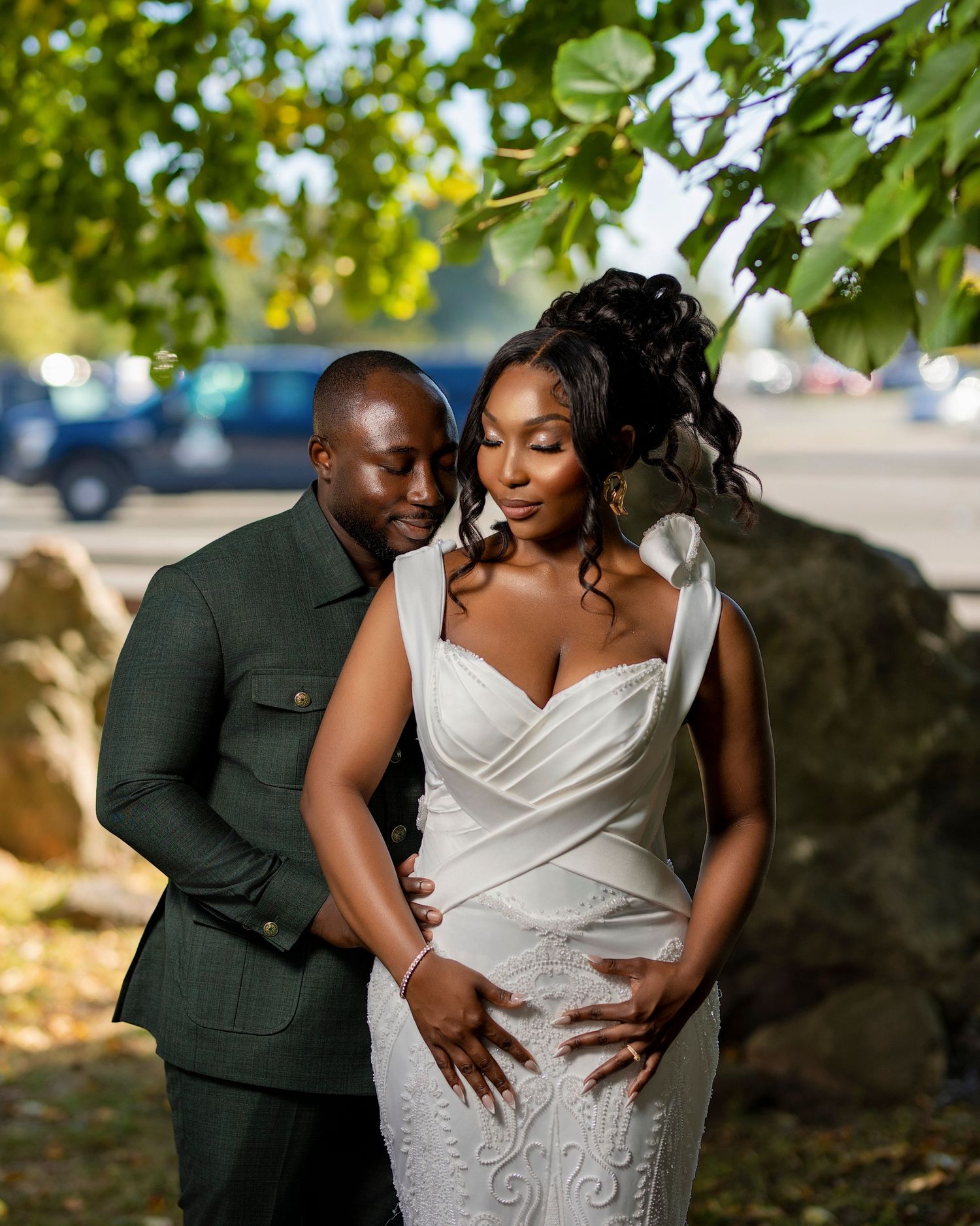 Couple poses for romantic wedding photos under tree branches in natural lighting.