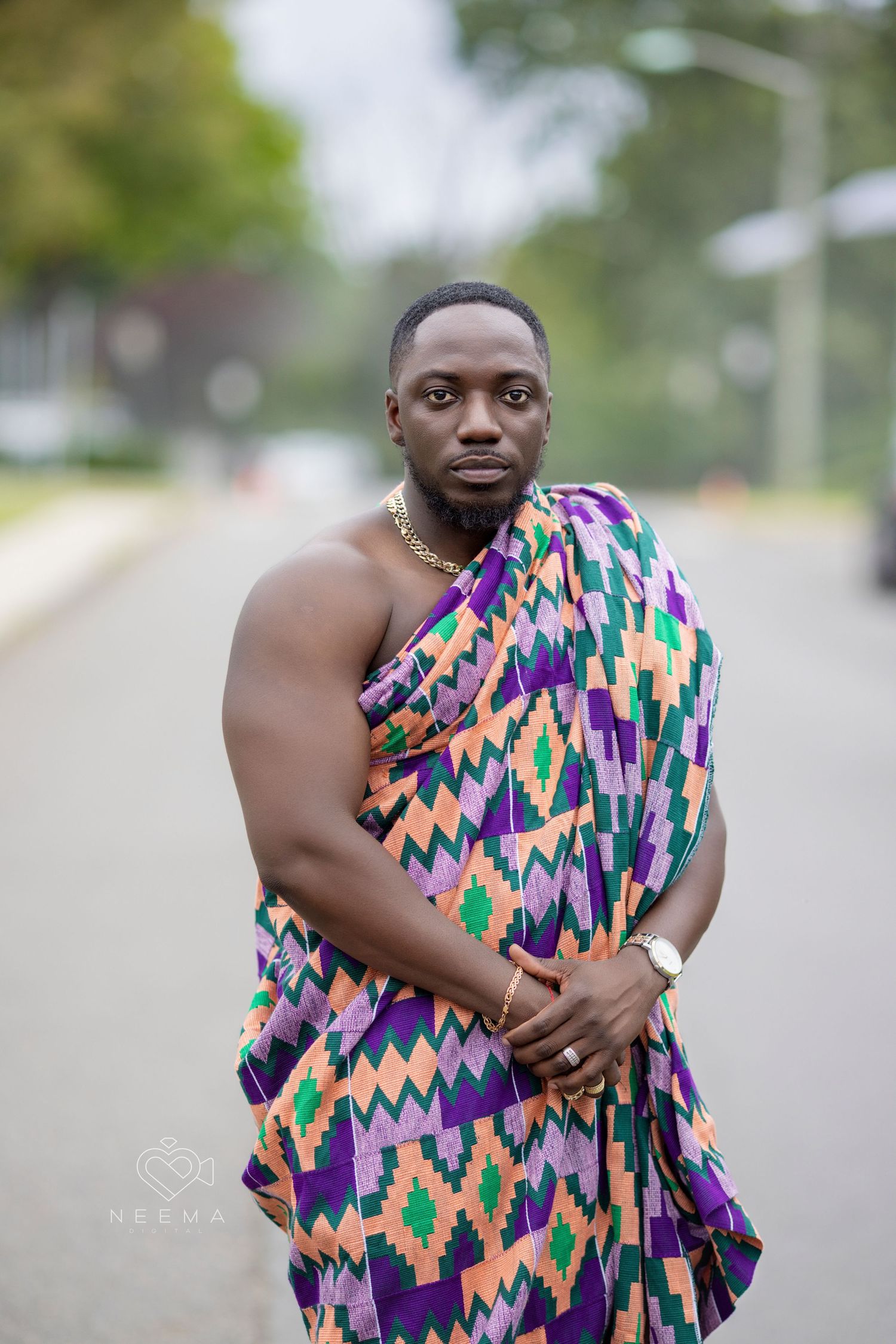 Man wearing colorful geometric patterned wrap poses on outdoor path.
