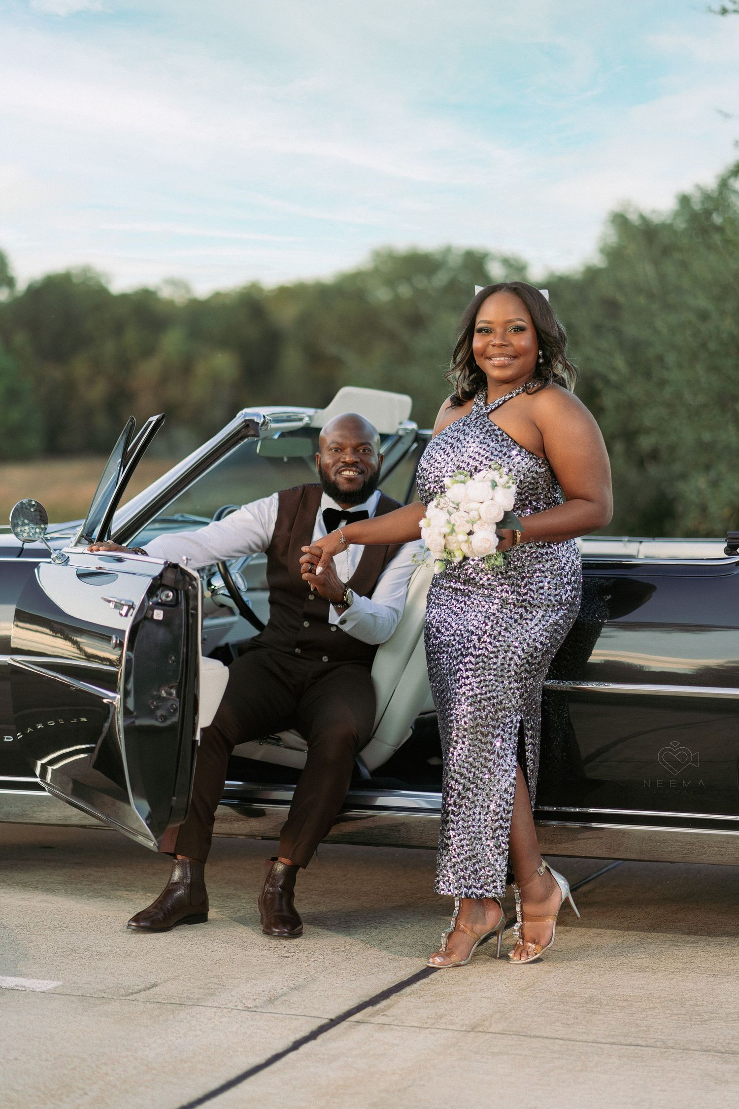 Couple posing with vintage black convertible car, wearing formal attire.