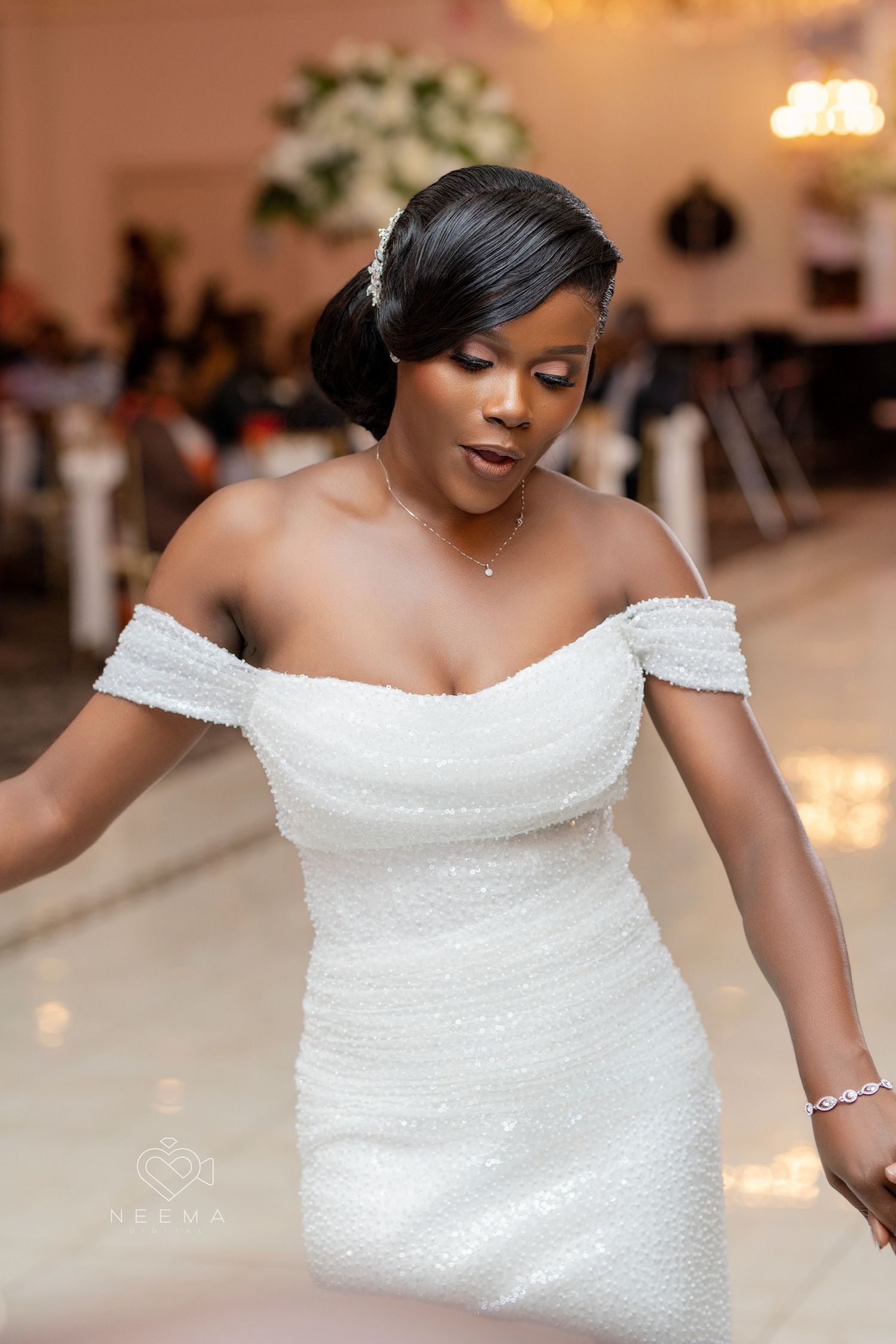 A bride in an off-shoulder white sequined wedding dress dances at her reception.