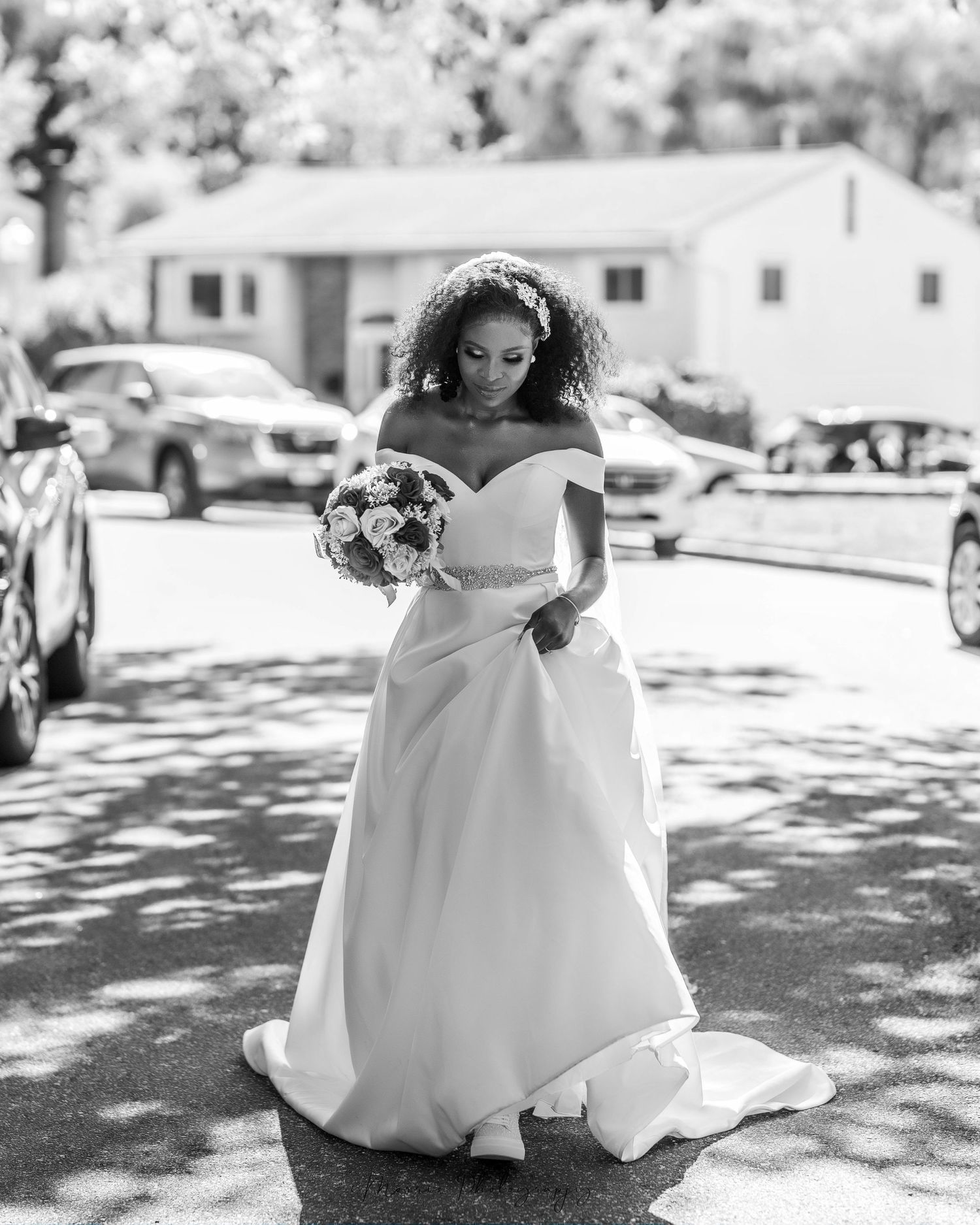 A bride in an elegant white off-shoulder wedding gown holds a bouquet outdoors.