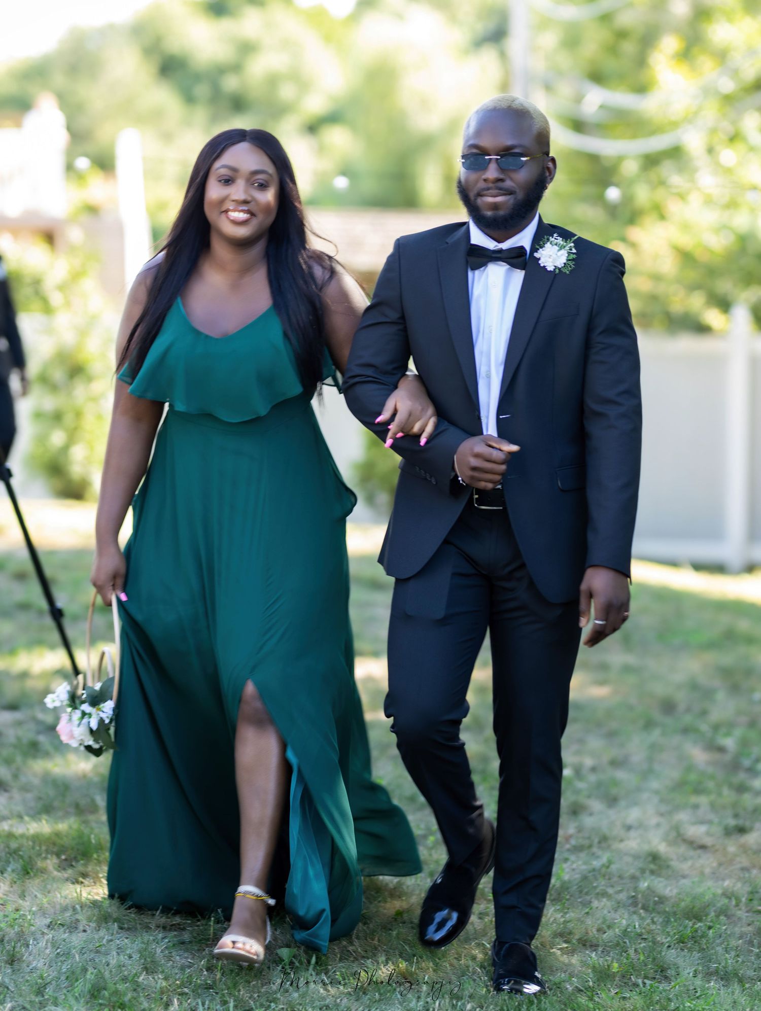 A couple walking arm in arm, with one in emerald green dress and other in classic tuxedo.
