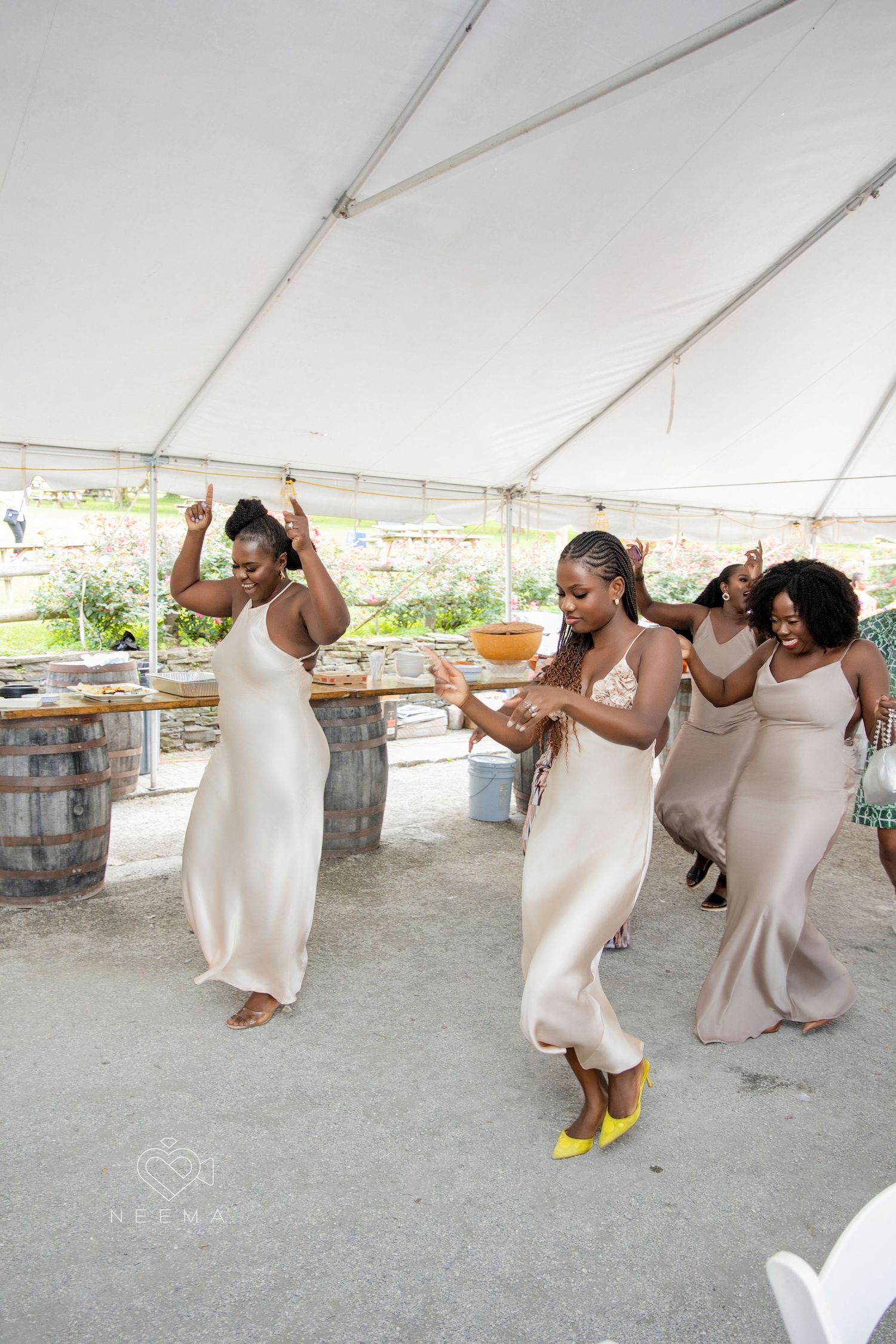 Wedding party dancing in matching cream-colored dresses at an outdoor reception.