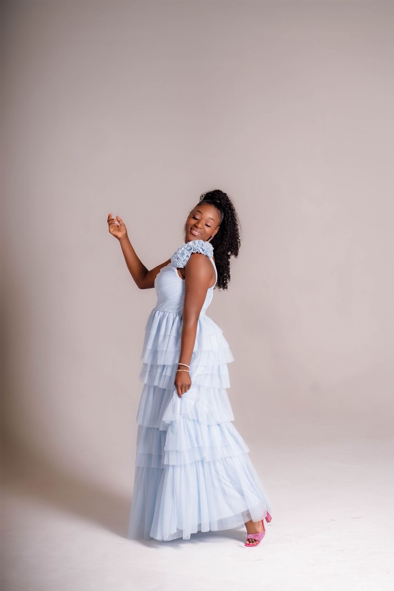 Elegant light blue tiered tulle gown worn in a portrait studio setting against a neutral backdrop.