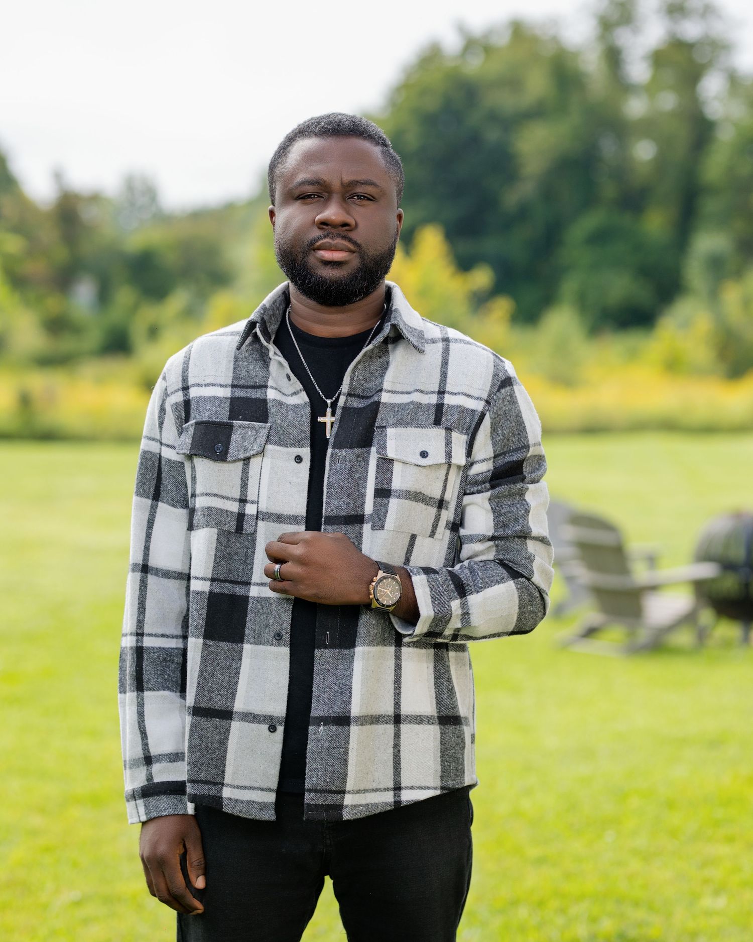 Casual outdoor portrait showing person in black and white plaid shirt jacket against green landscape.