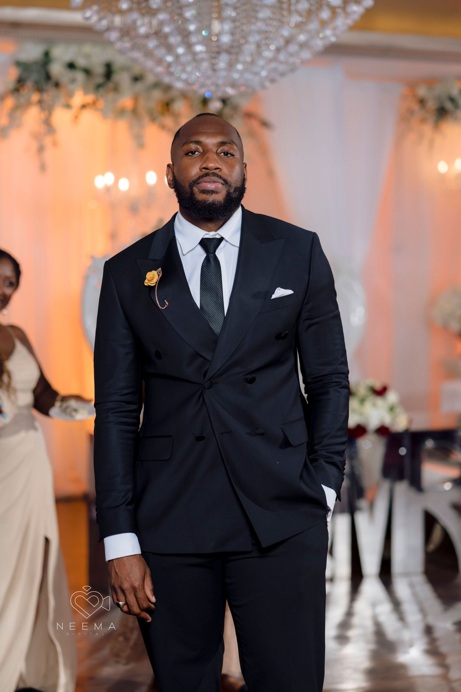 A formal portrait of a groom in a classic black tuxedo at an elegant wedding reception.