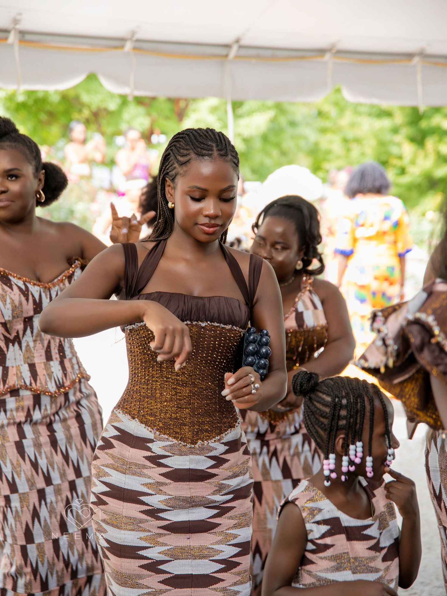 Wedding guests dancing in traditional African print dresses at an outdoor celebration.