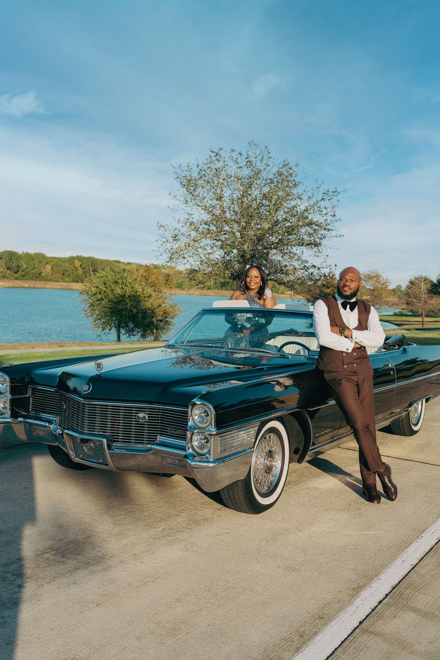 Stylish couple posing with classic Cadillac convertible by lakeside.