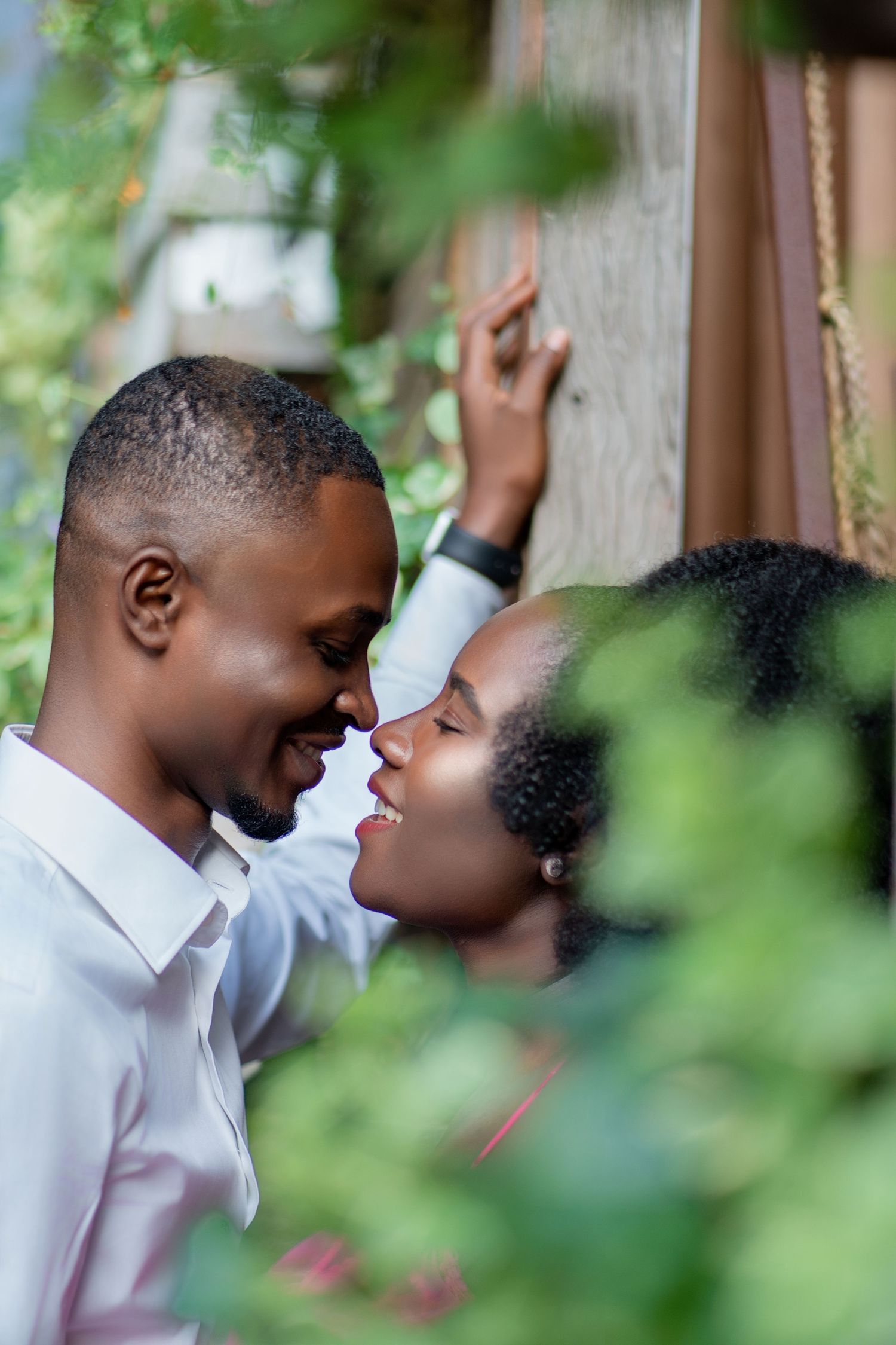 Intimate portrait of a couple sharing a tender moment framed by green foliage.