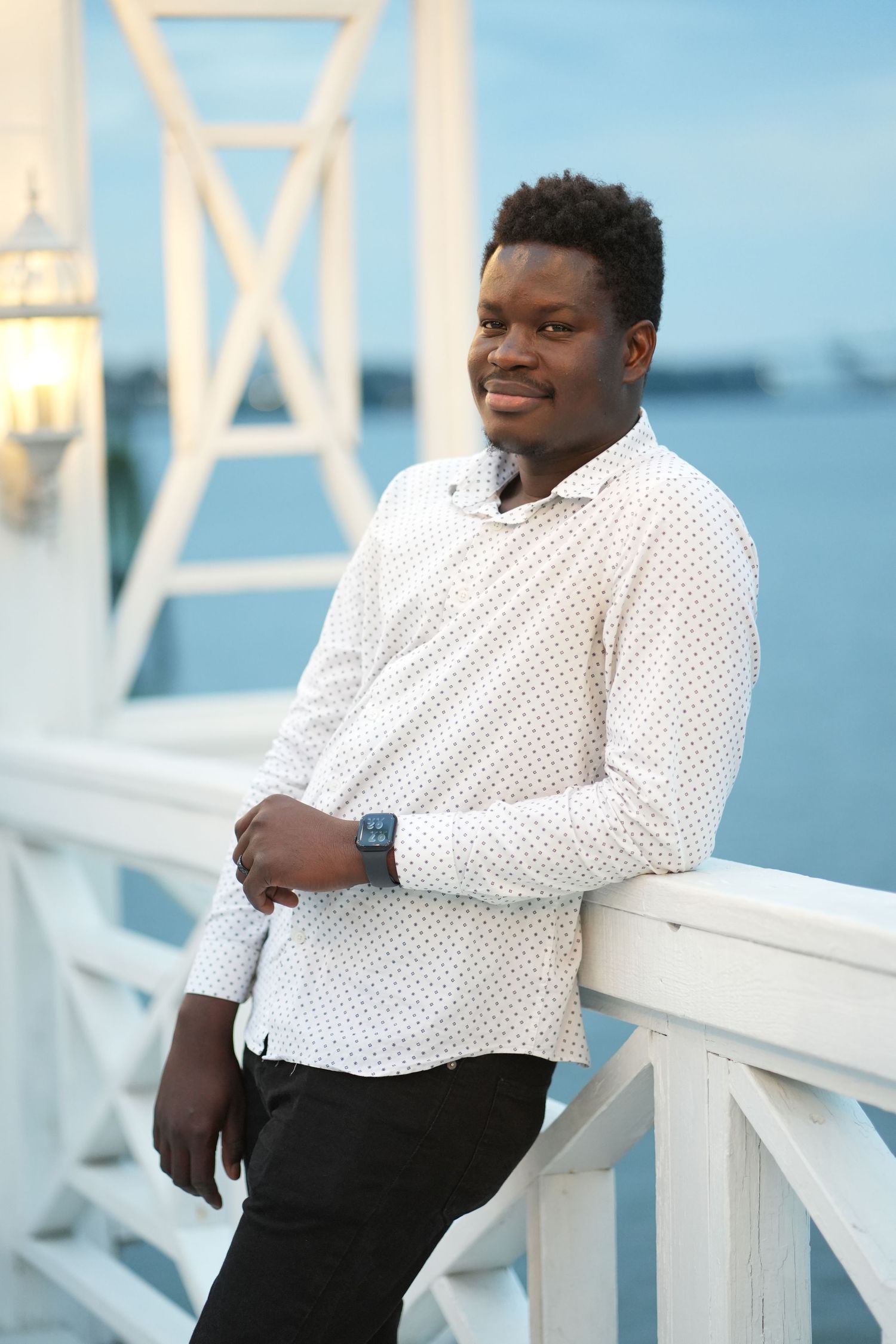 Professional portrait of a person in a white polka dot shirt posing against a white railing outdoors.
