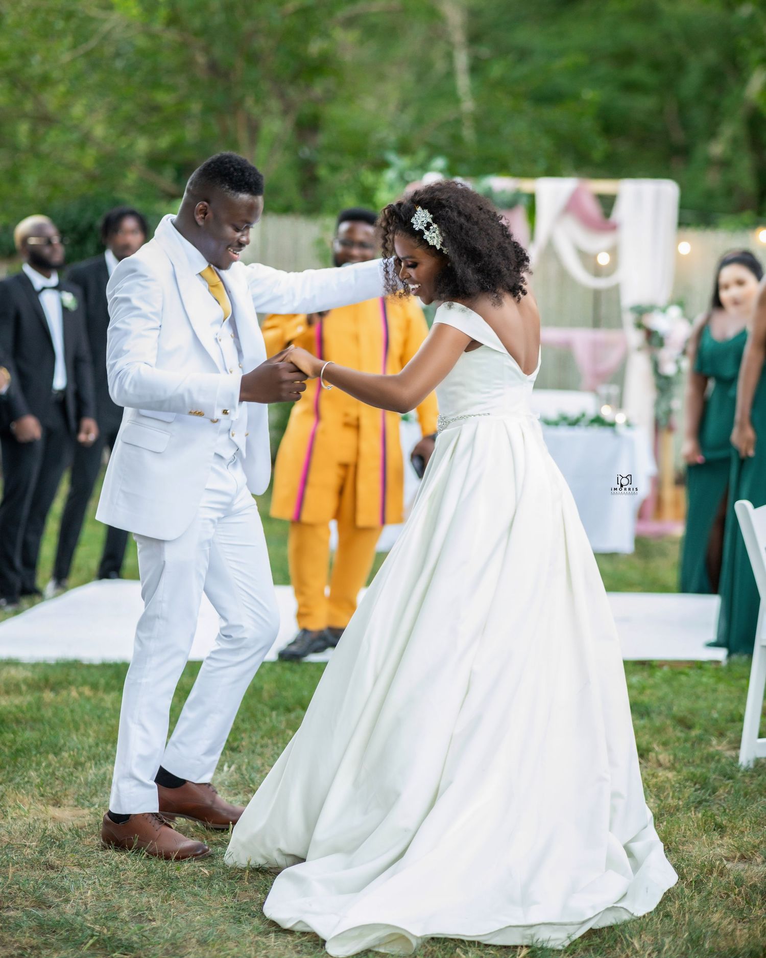 A couple in white attire dances at an outdoor wedding celebration.