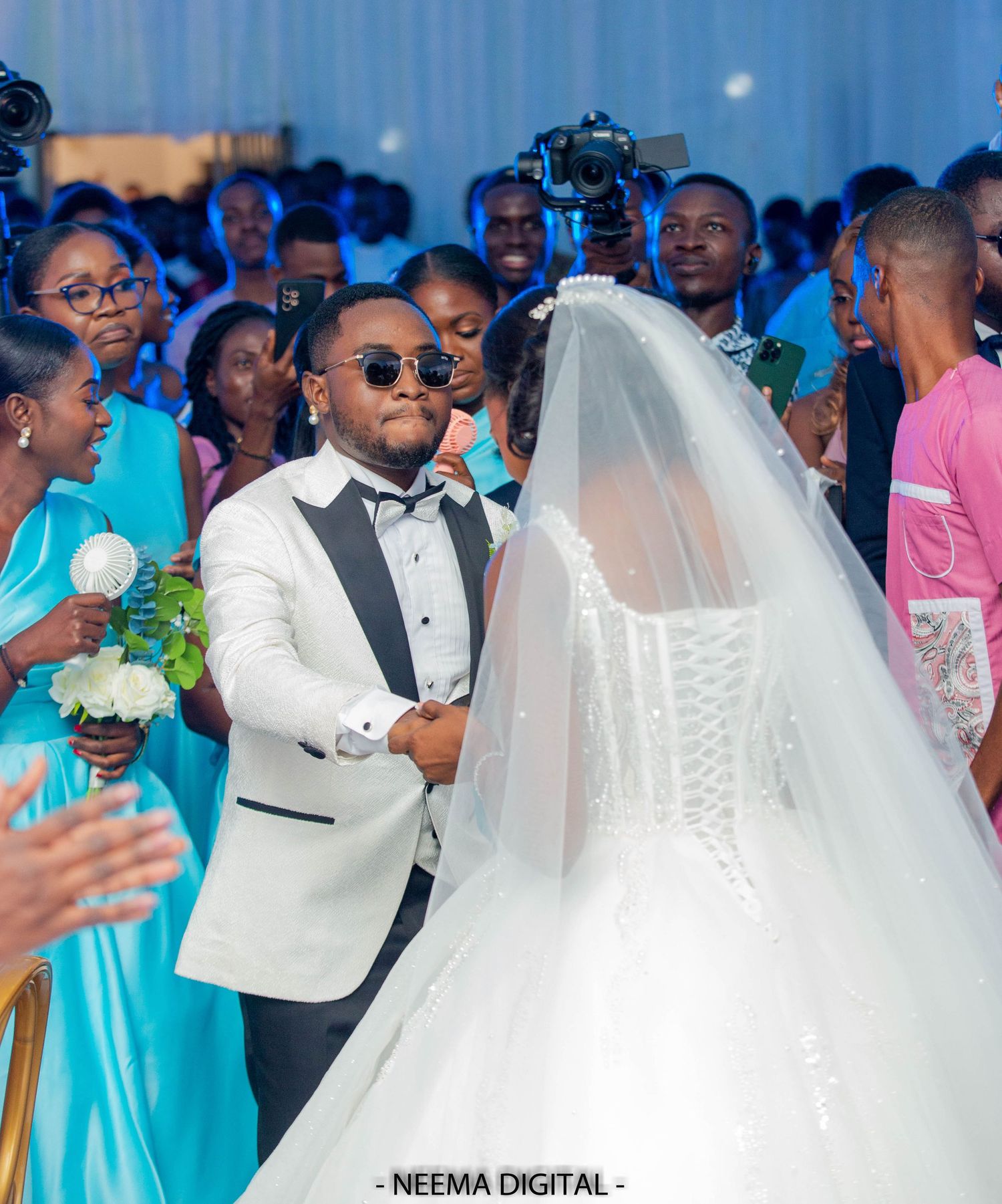 Wedding ceremony scene with guests in blue attire and a couple at the altar.