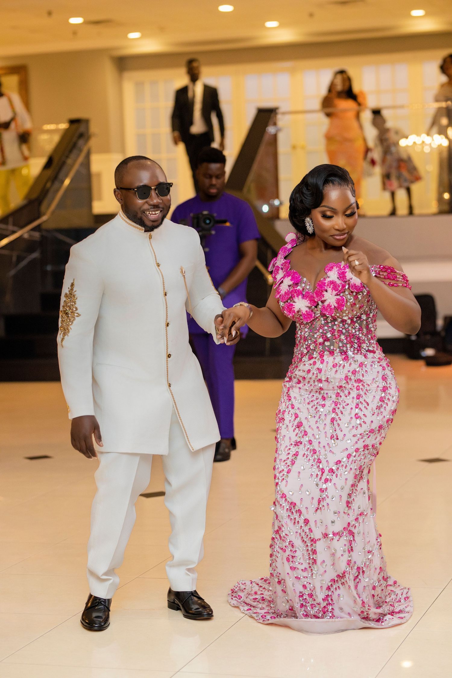 Wedding reception celebration with couple dancing in white suit and pink sequined gown.