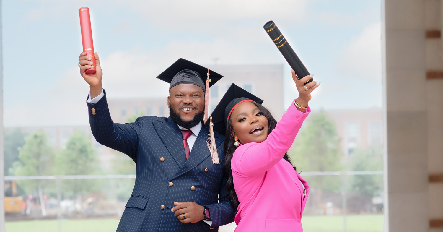 Two graduates holding up their diplomas while celebrating in academic regalia.