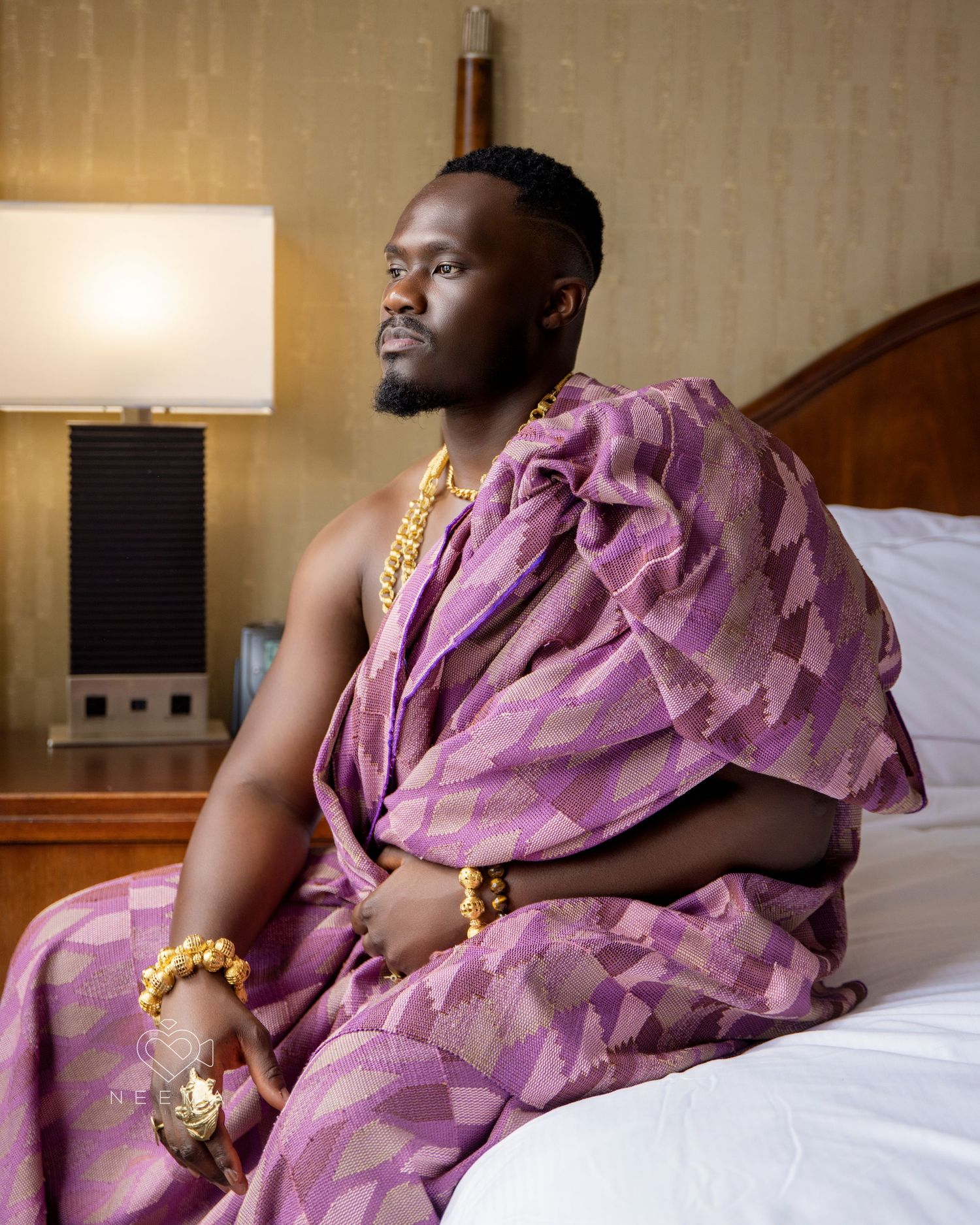 Person wearing purple silk formal attire poses regally on a bed.