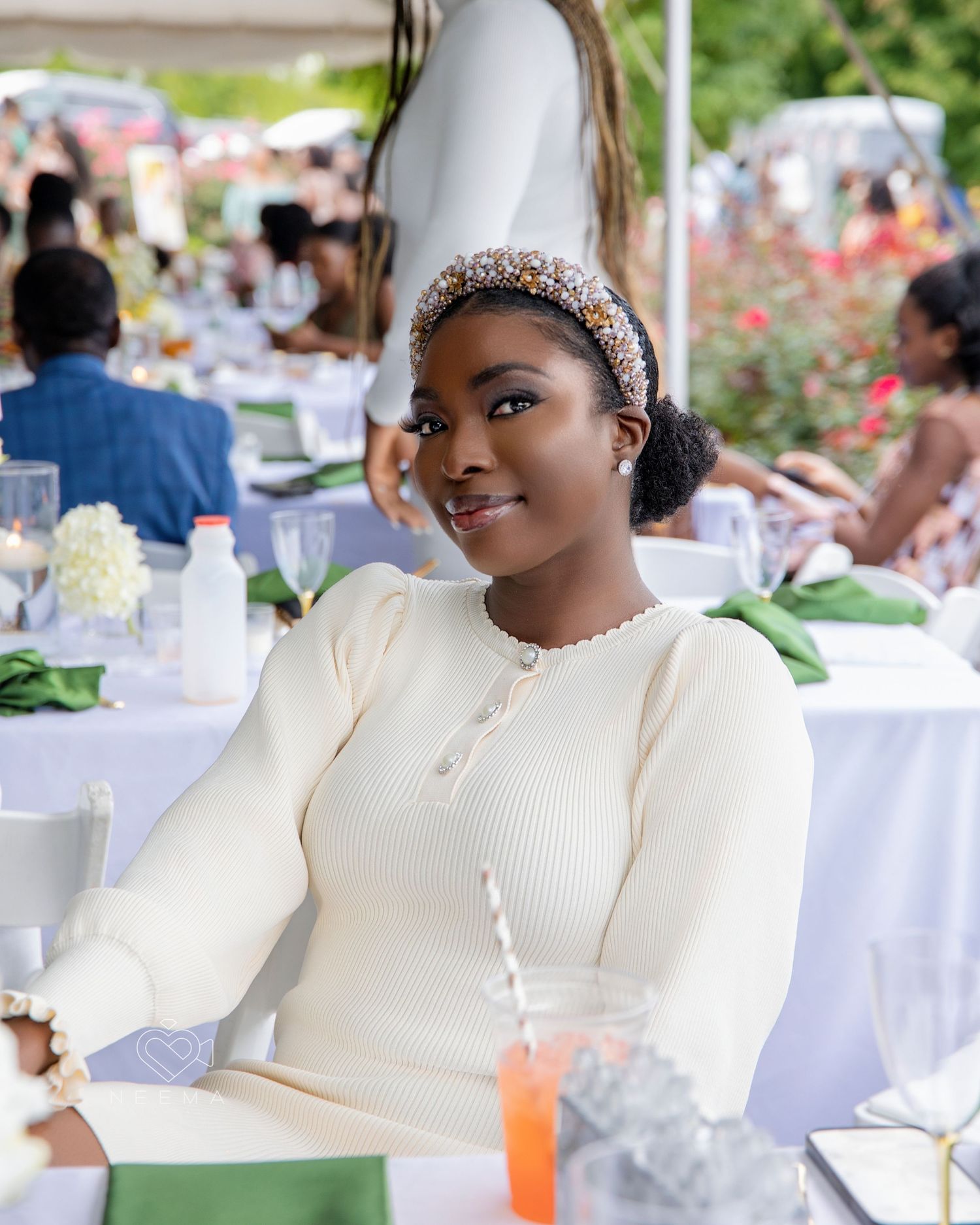Elegant wedding guest in a cream sweater and headband at an outdoor reception.