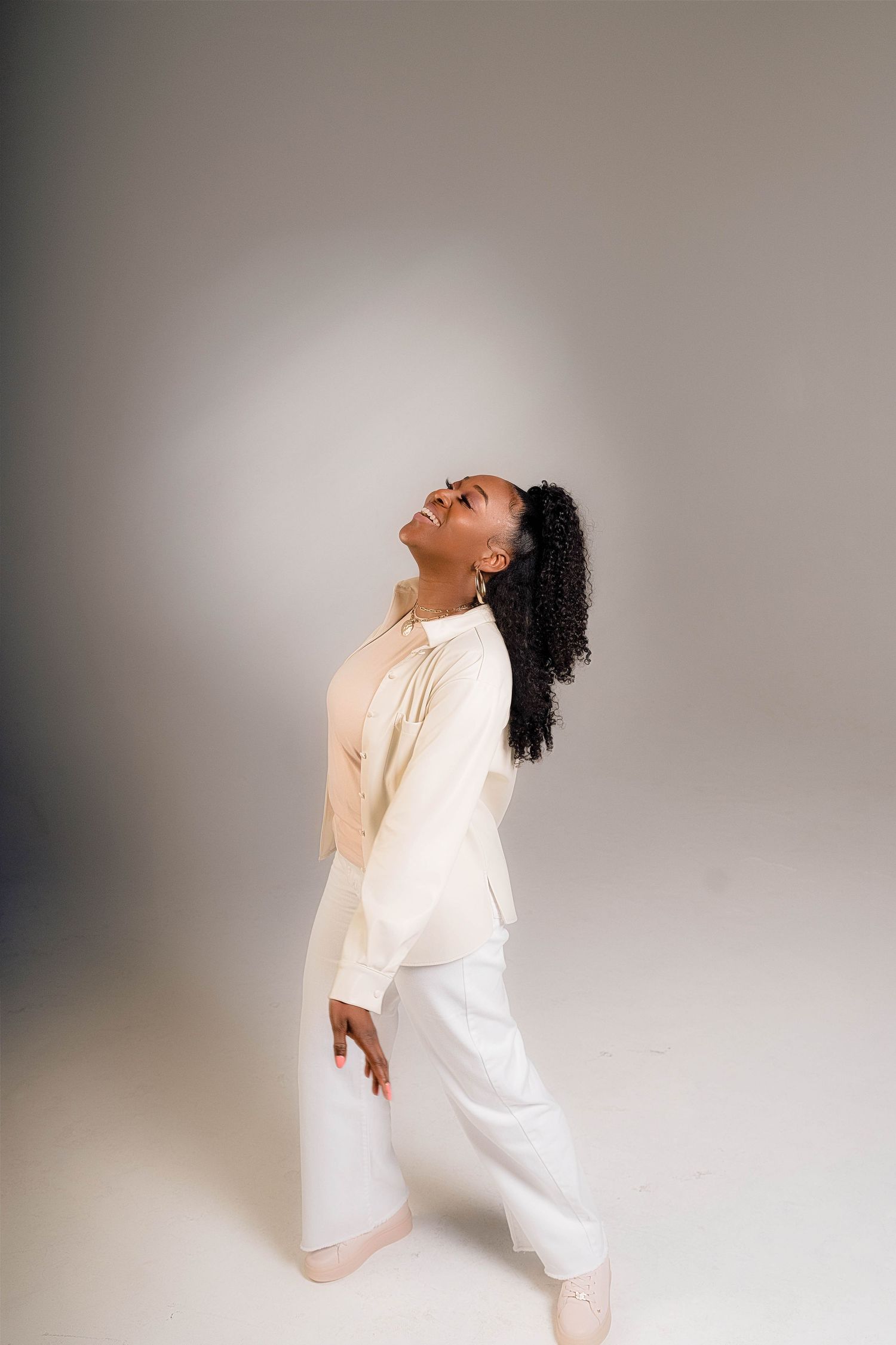 Dancer in white clothing performs graceful movement against studio backdrop.