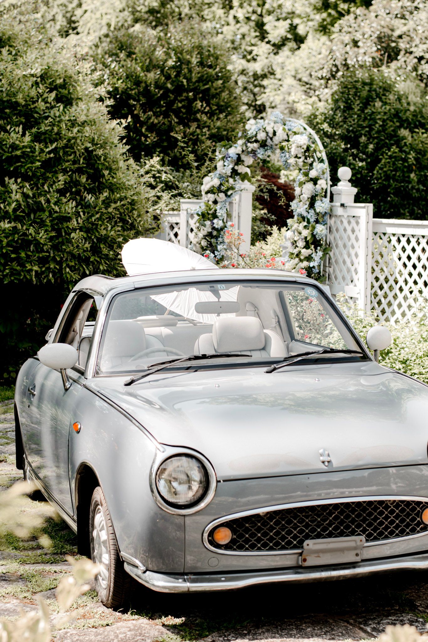 A vintage blue car parked in front of a garden arbor with white lattice and floral decorations Wildflower 301 Venue in Greensboro, Georgia