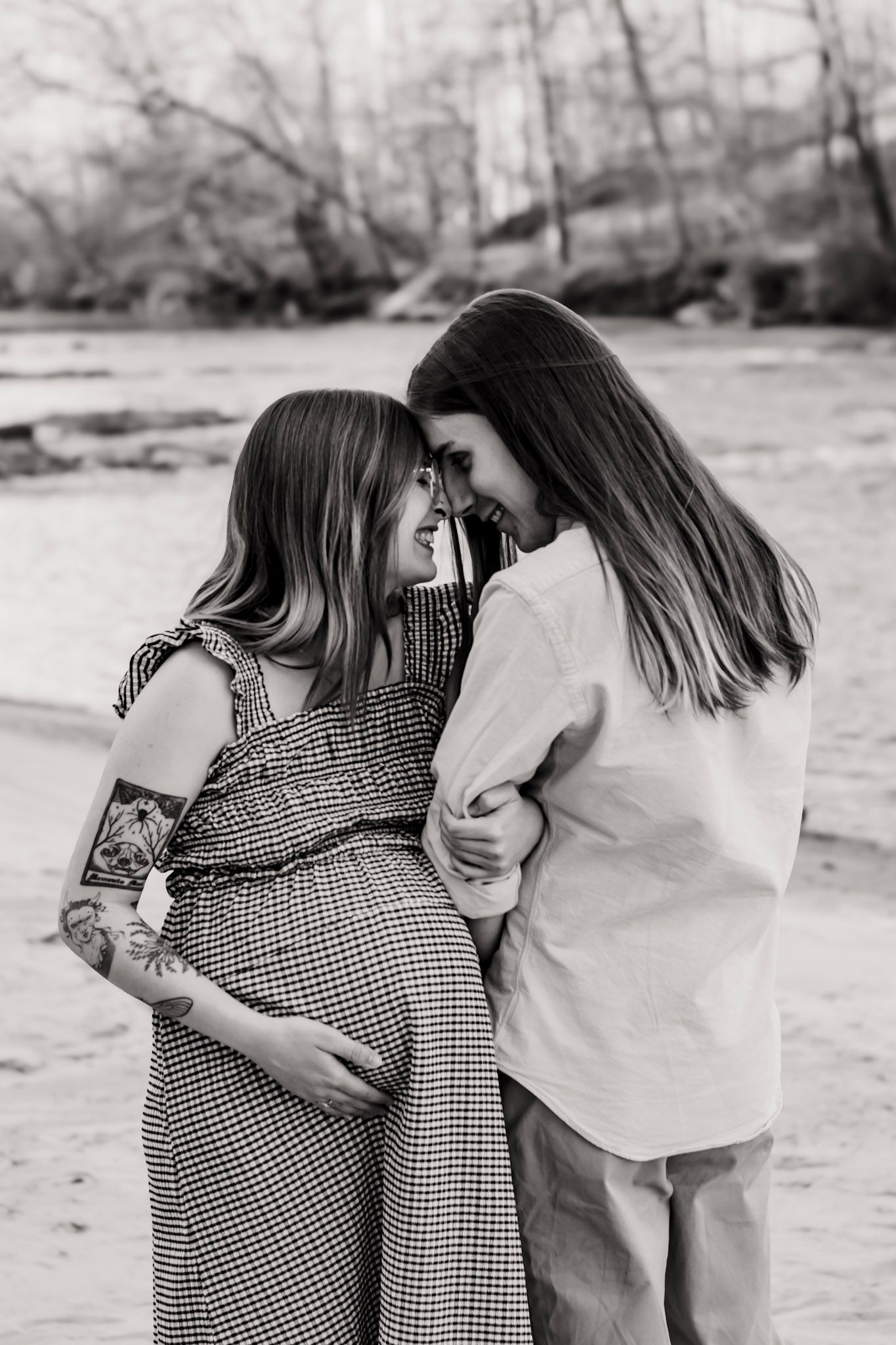 A  black and white photo of a couples session in a gingham dress and white shirt embracing outdoors at Sweetwater State Park in Georgia