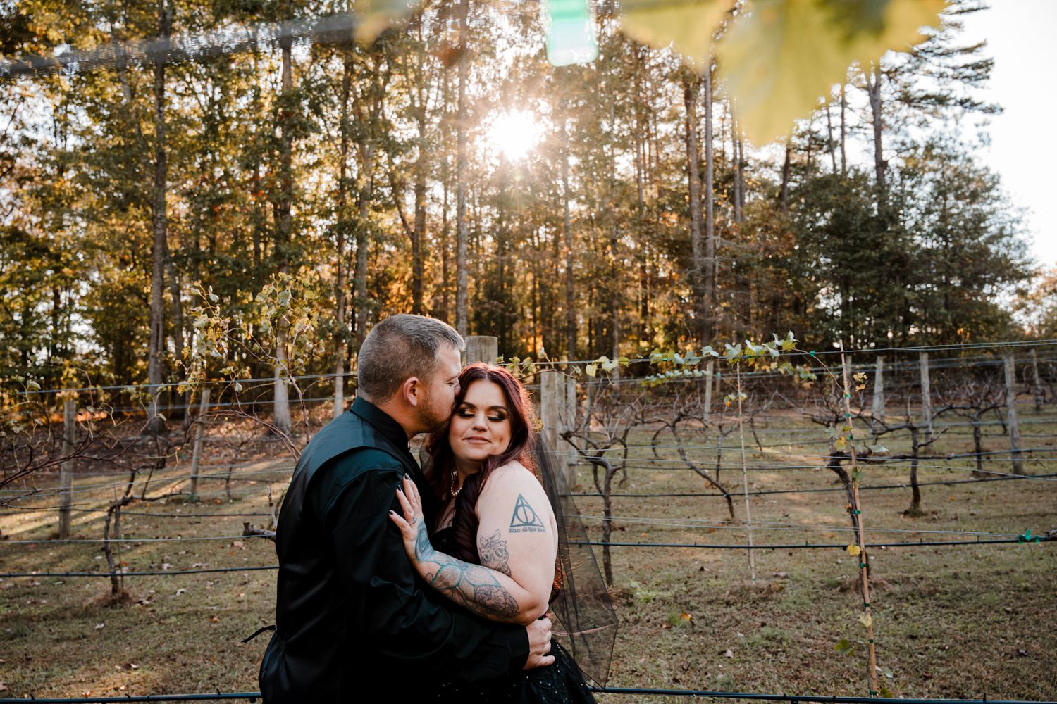 A couple embraces in a sunlit vineyard during golden hour as sunlight streams through Koury Farms in  Auburn, Georgia.