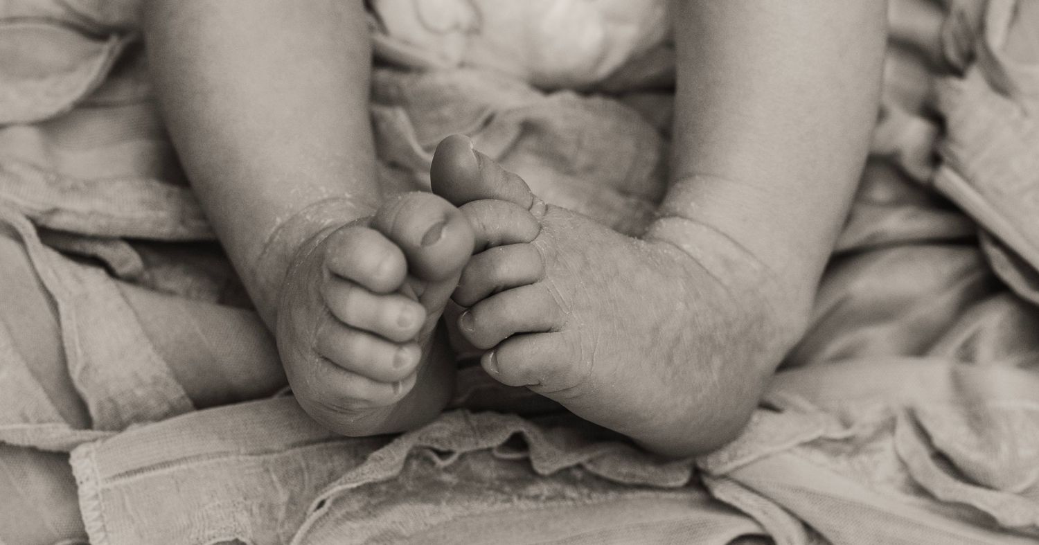 A close-up black and white photograph shows tiny baby feet resting on soft fabric bedding in Covington, GA