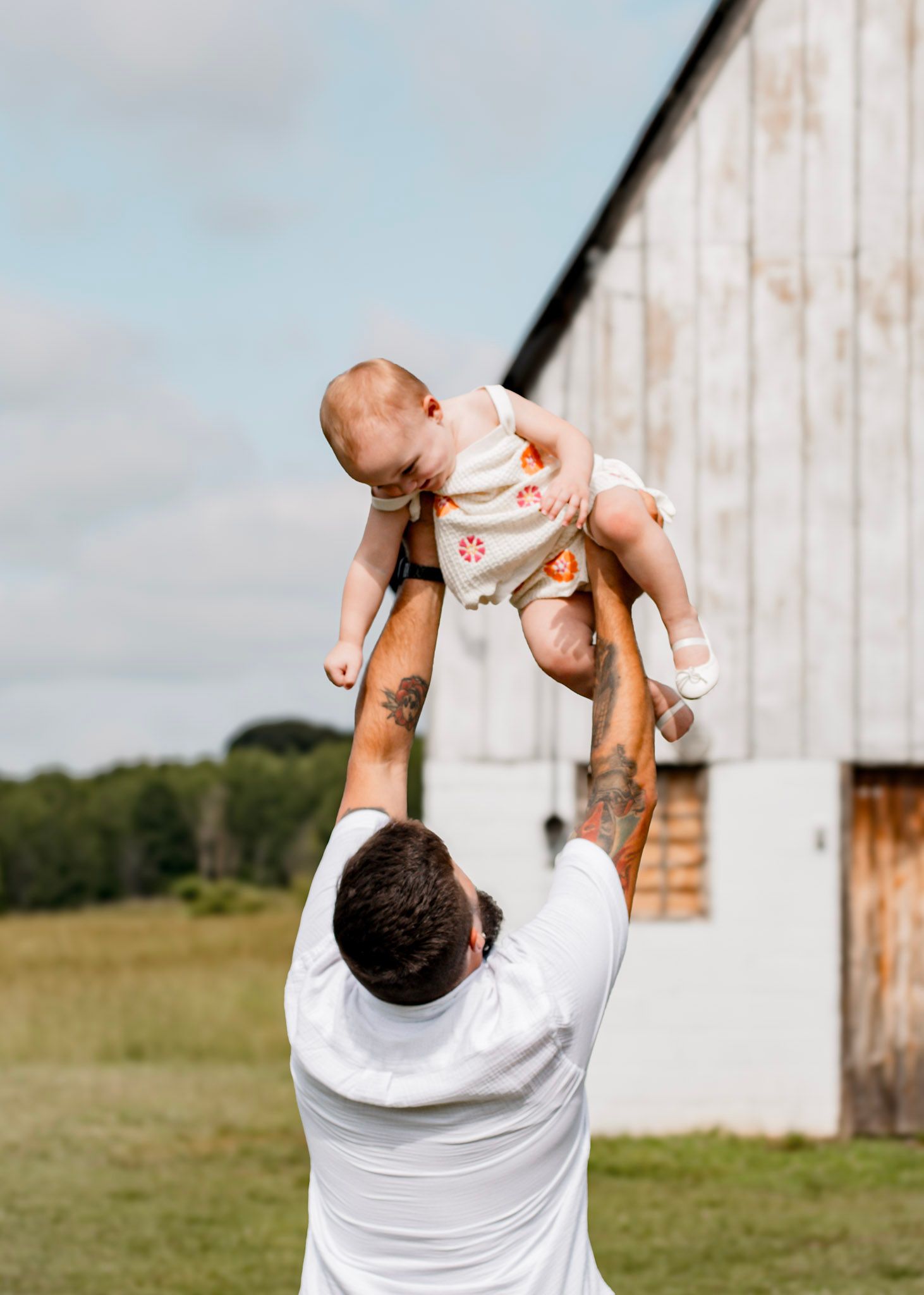 A father lifts a baby up in the air while standing in a field with wooden posts visible maternity session at Vaughter's Farm in Lithonia, GA