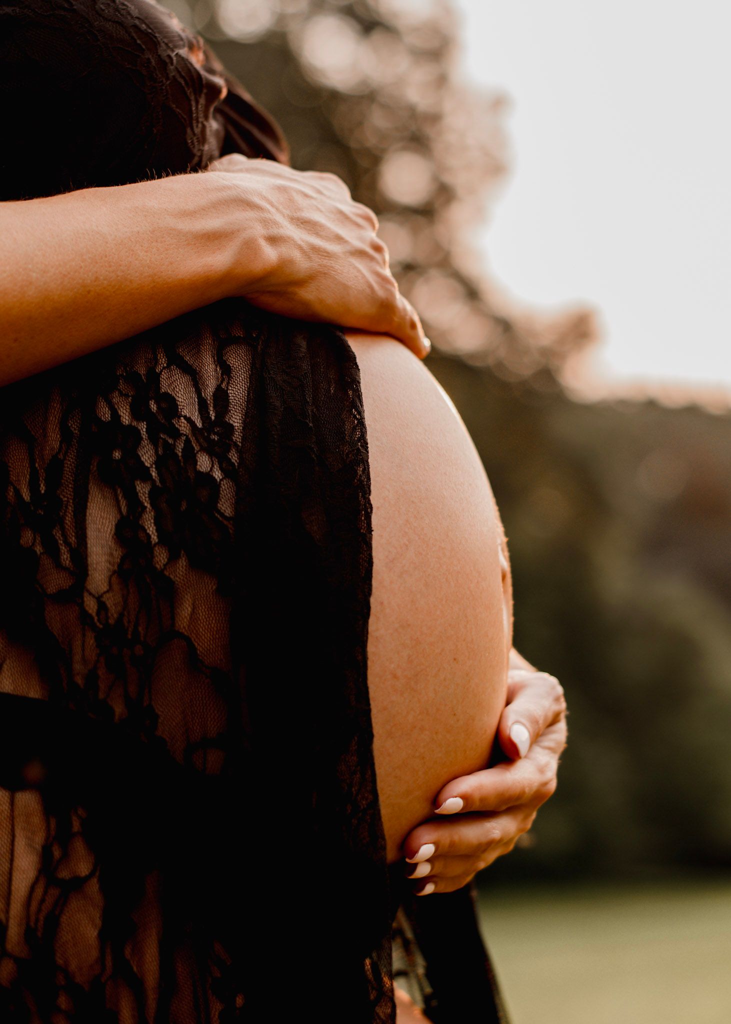 Maternity photos show a pregnant woman's belly in black lace against a warm sunset background at Kennesaw Mountain in Kennesaw, Georgia