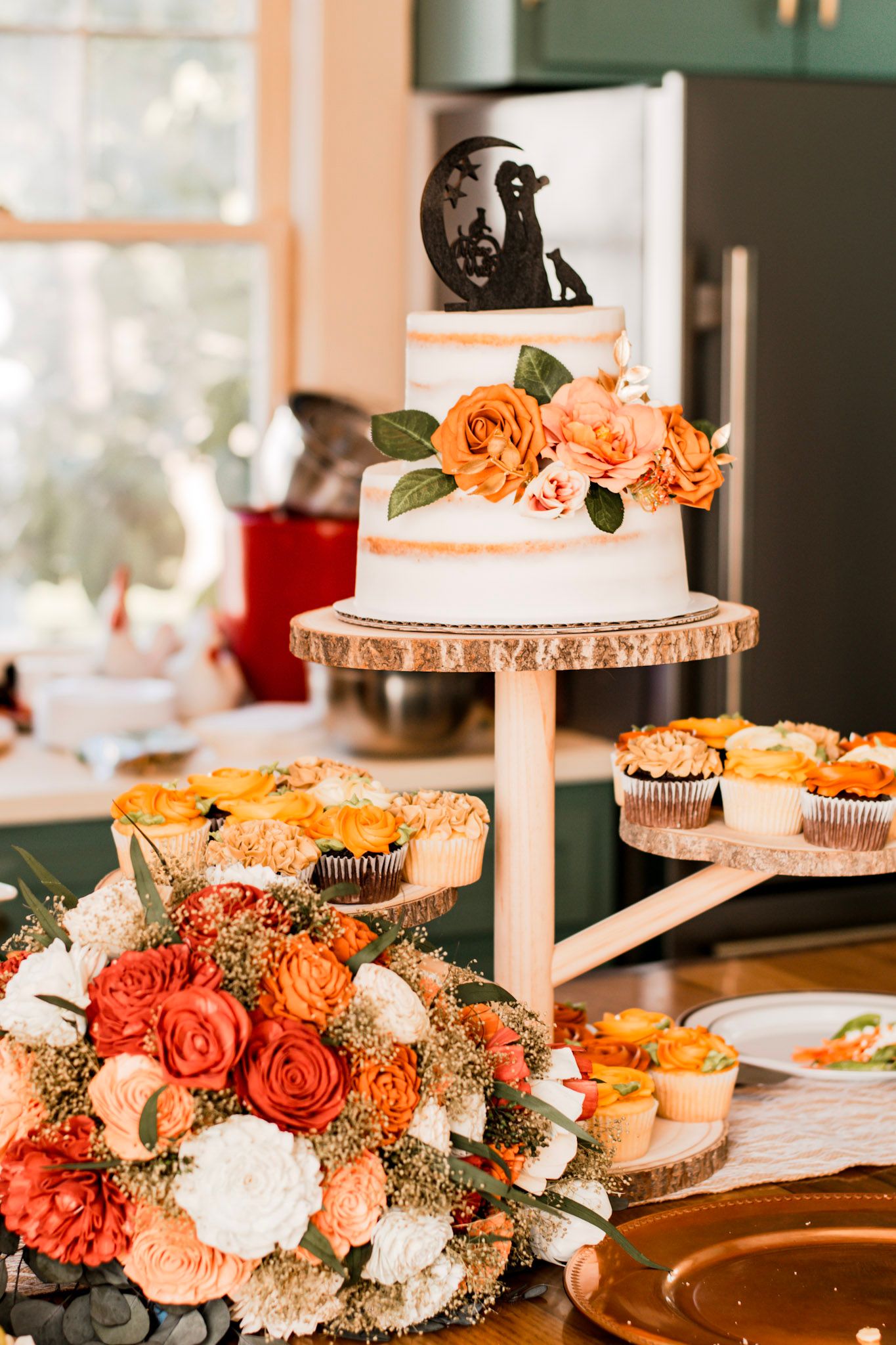 Elegant dessert display with pink and coral floral arrangements, cupcakes, and tiered serving platters on a rustic table in Albany, Georgia.