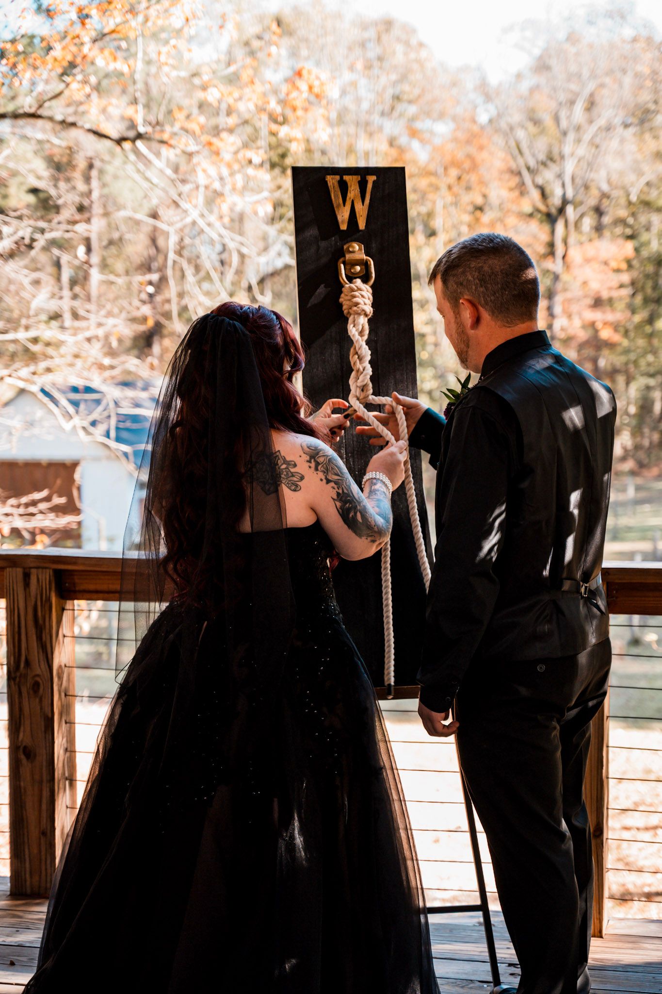 A bride and groom stand at an outdoor ceremony site with autumn foliage in the background c