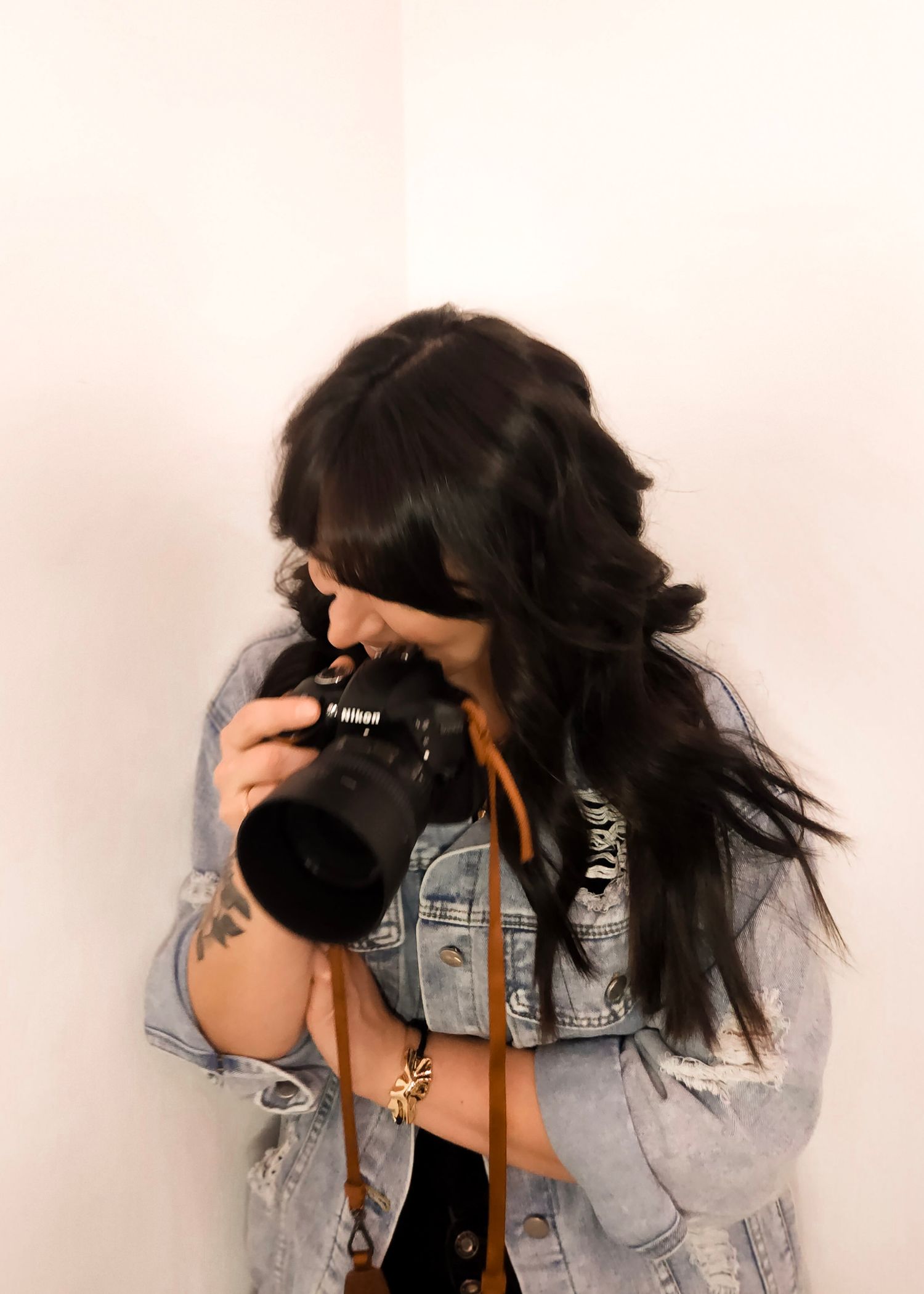 Emily Hall Photographer in denim jacket holding professional Nikon camera against white background.