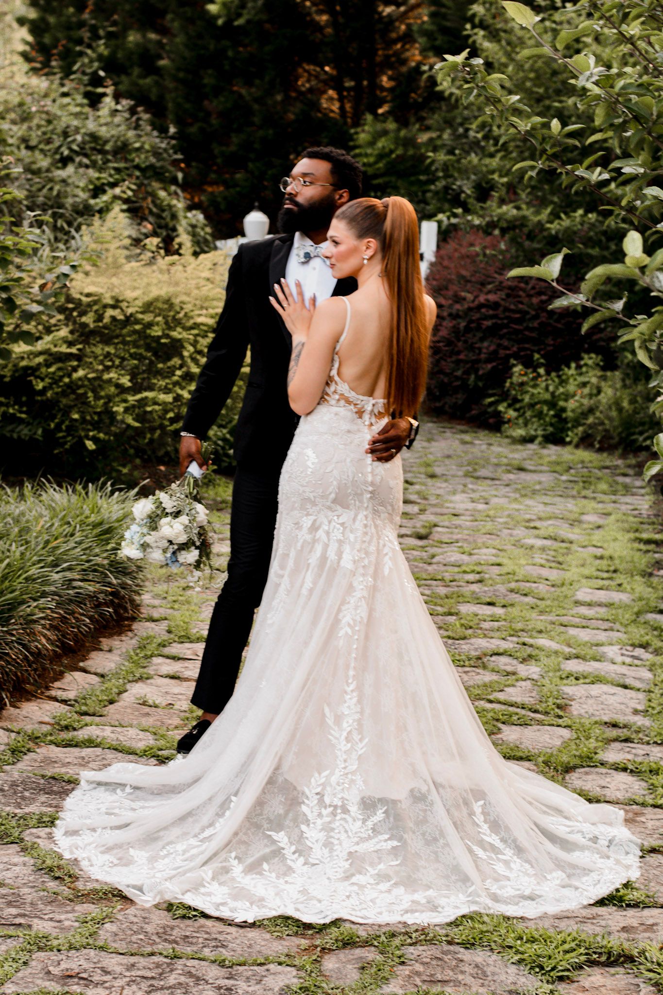 A romantic wedding couple on a stone pathway surrounded by lush garden greenery  Wildflower 301 Venue in Greensboro, Georgia
