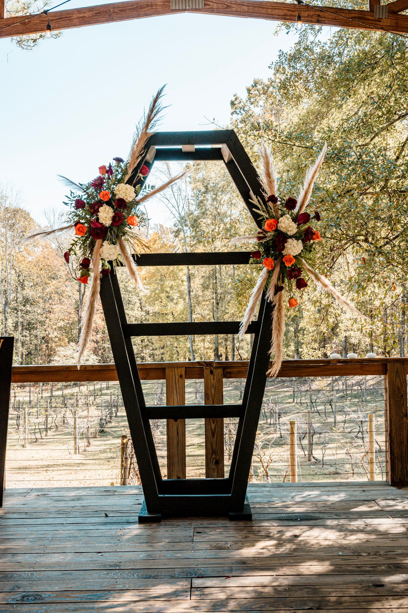 Modern black wedding arch decorated with autumn floral arrangements and pampas grass on outdoor wooden deck Koury Farms in  Auburn, Georgia.