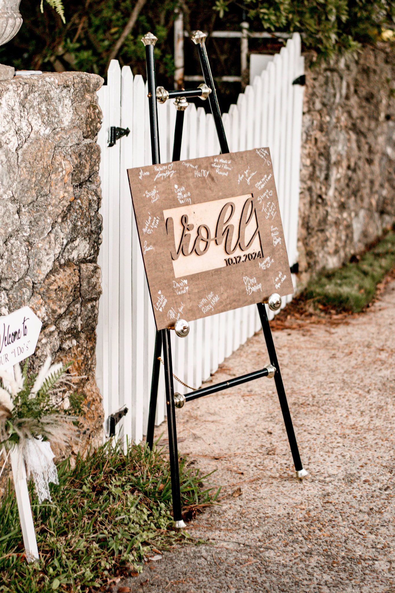 Rustic wooden signs with handwritten text displayed on black easels along a gravel path next to a white picket fence in Albany, Georgia.