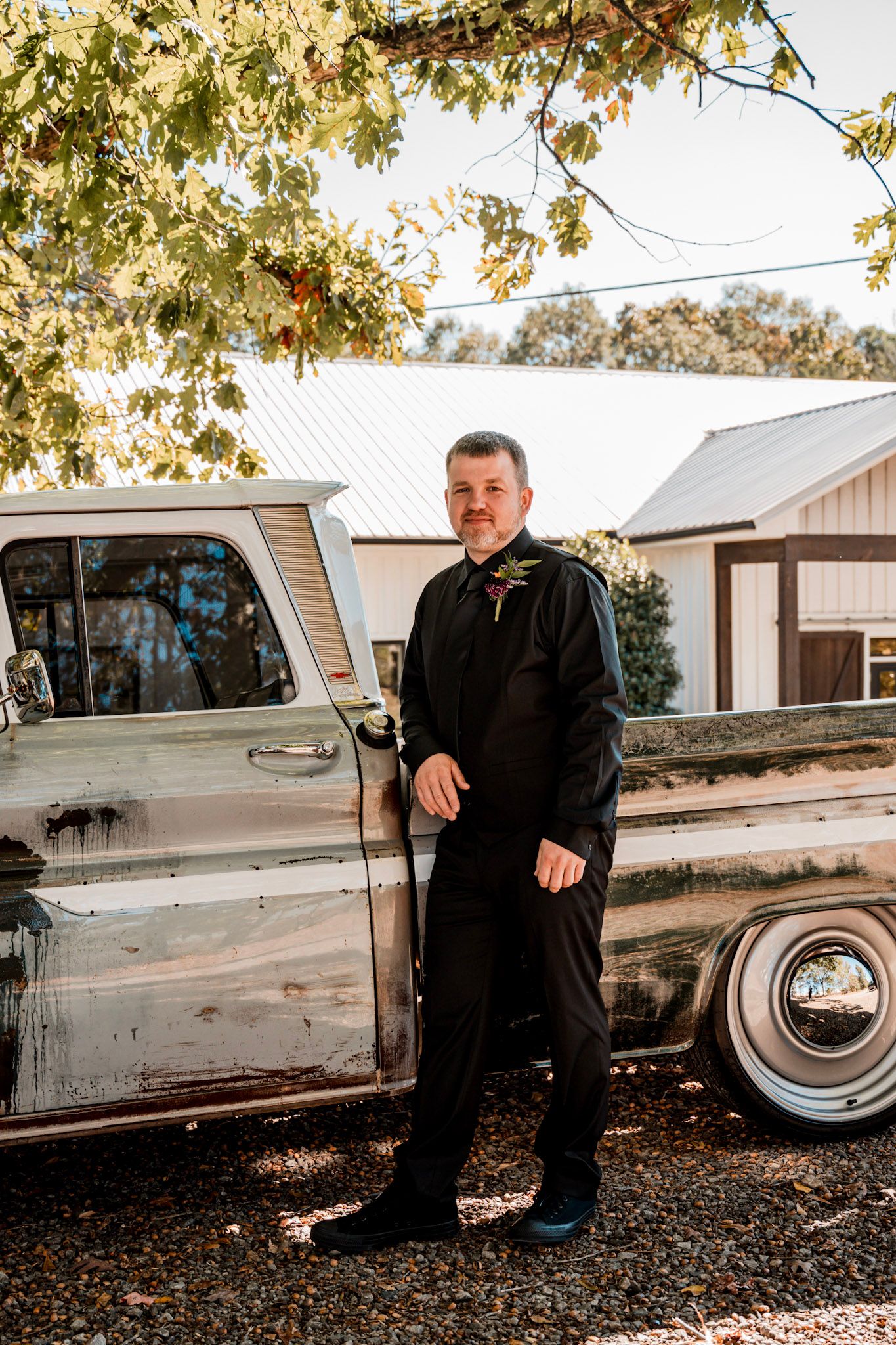 Classic truck parked under autumn trees with groom in black suit standing beside it at Koury Farms in Auburn, Georgia.