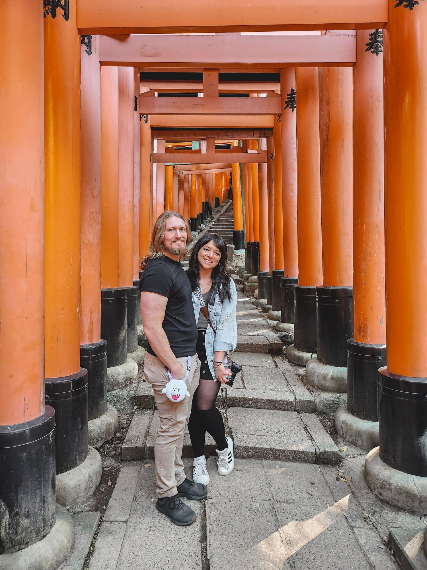 Emily Hall and Husband walk through vibrant orange torii gates at Fushimi Inari Shrine in Kyoto, Japan.
