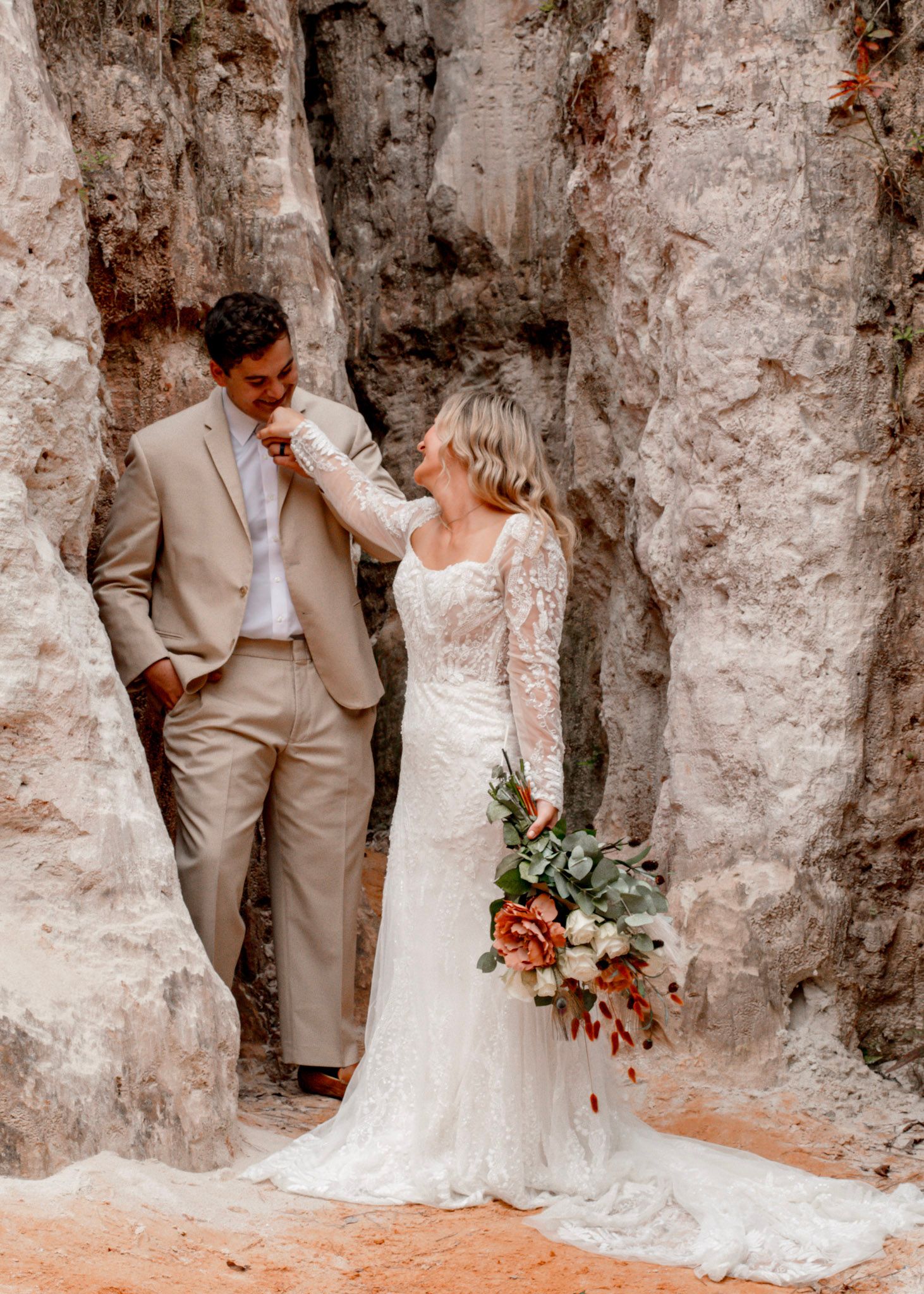 A romantic wedding couple poses against a textured stone wall in at Providence Canyon in Lumpkin, Georgia.