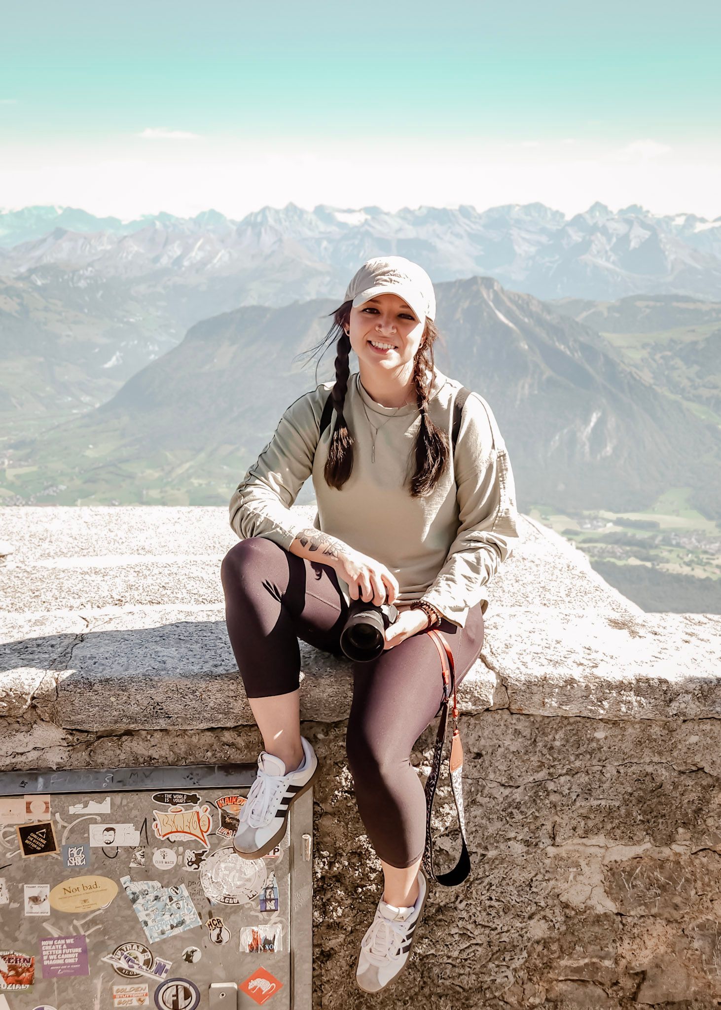 Emily Hall, photographer, in Switzerland on a stone wall taking photos of a scenic mountain landscape at Schilthorn  in Lauterbrunnen