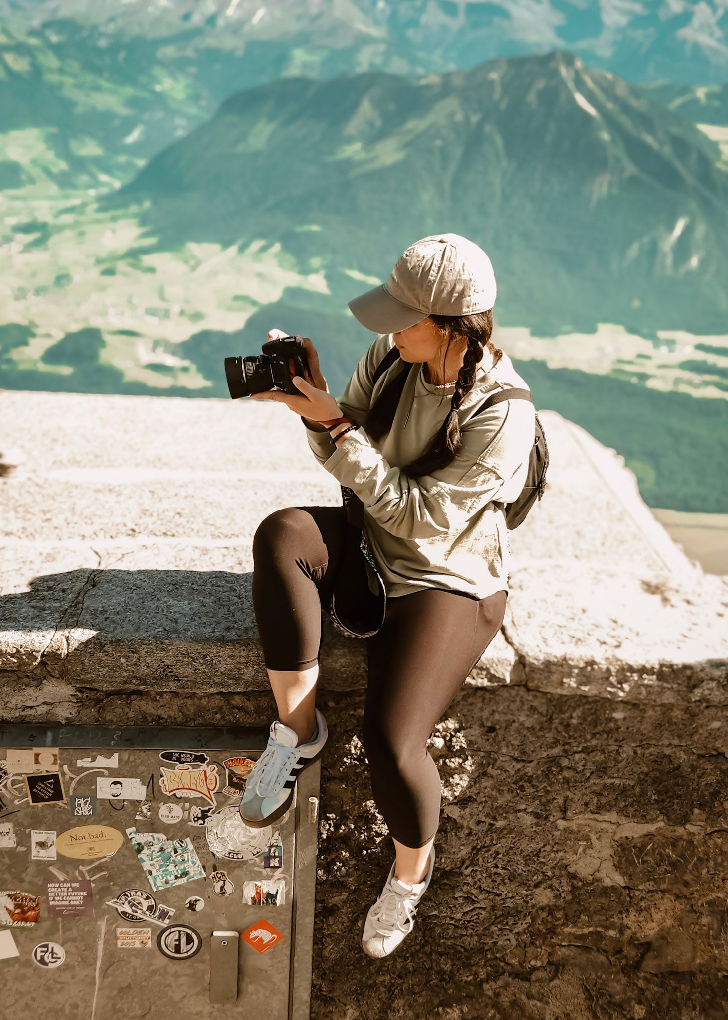Emily Hall, photographer, in Switzerland on a stone wall taking photos of a scenic mountain landscape at Schilthorn  in Lauterbrunnen