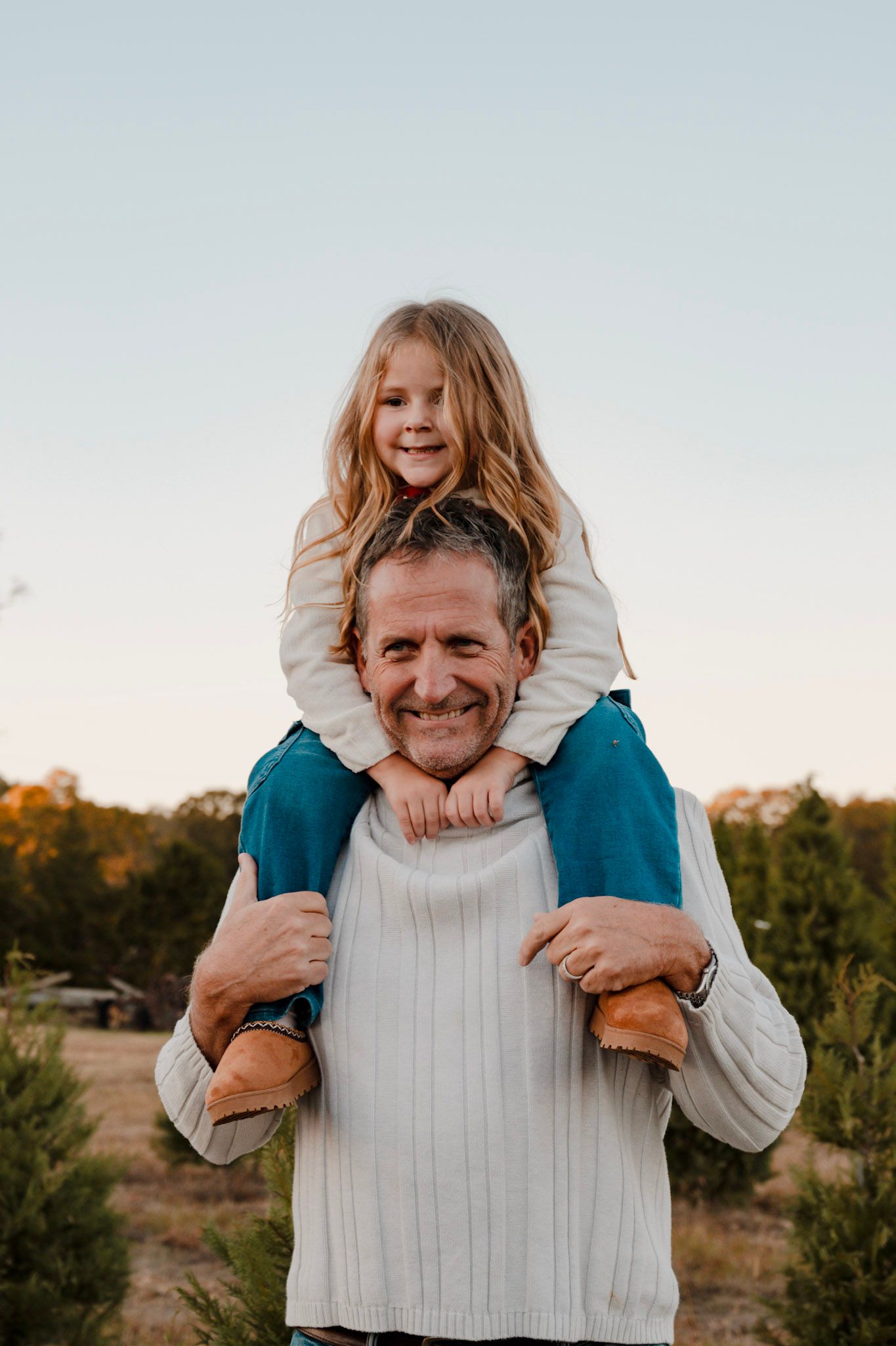 A parent and child share a joyful moment outdoors during golden hour as they pose for a shoulder ride portrait.