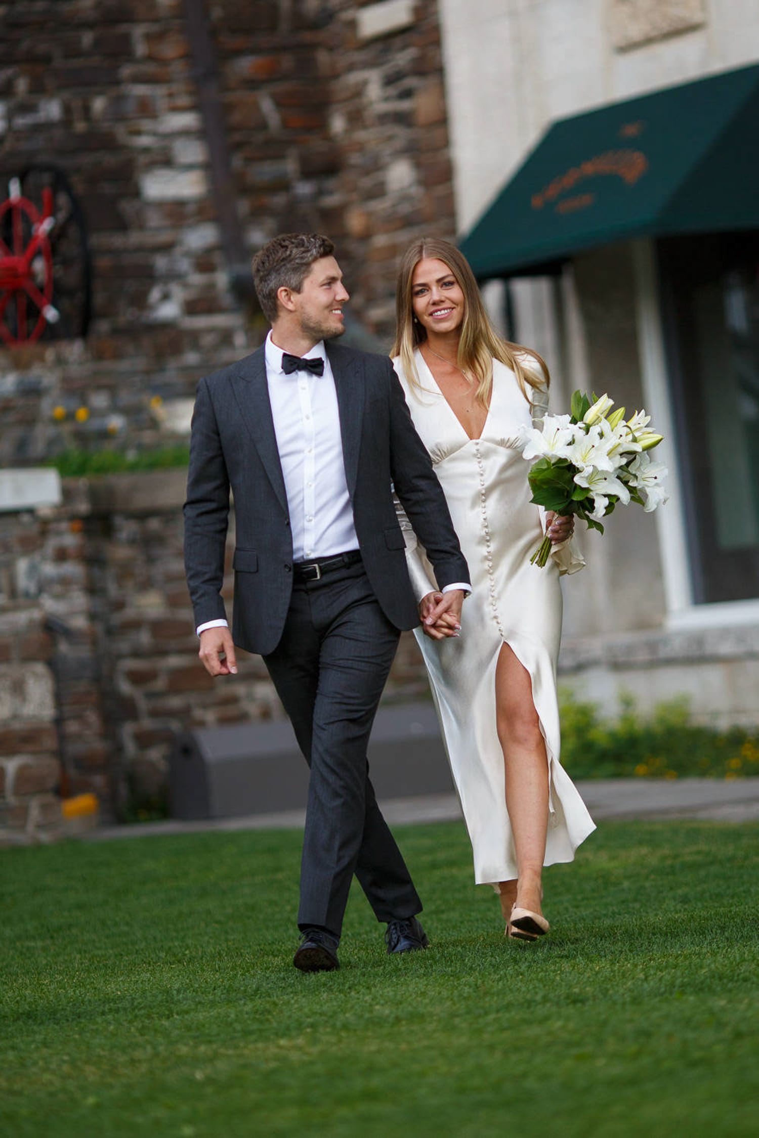 A couple in wedding attire walk together on a grassy lawn at the Fairmont Banff Springs Hotel in Banff.
