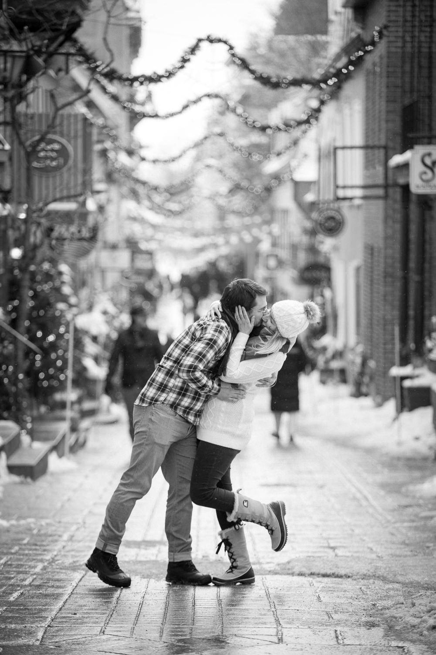 A romantic black and white photo sequence shows a couple sharing a sweet kiss on a cobblestone street in a charming town of Old Quebec City.