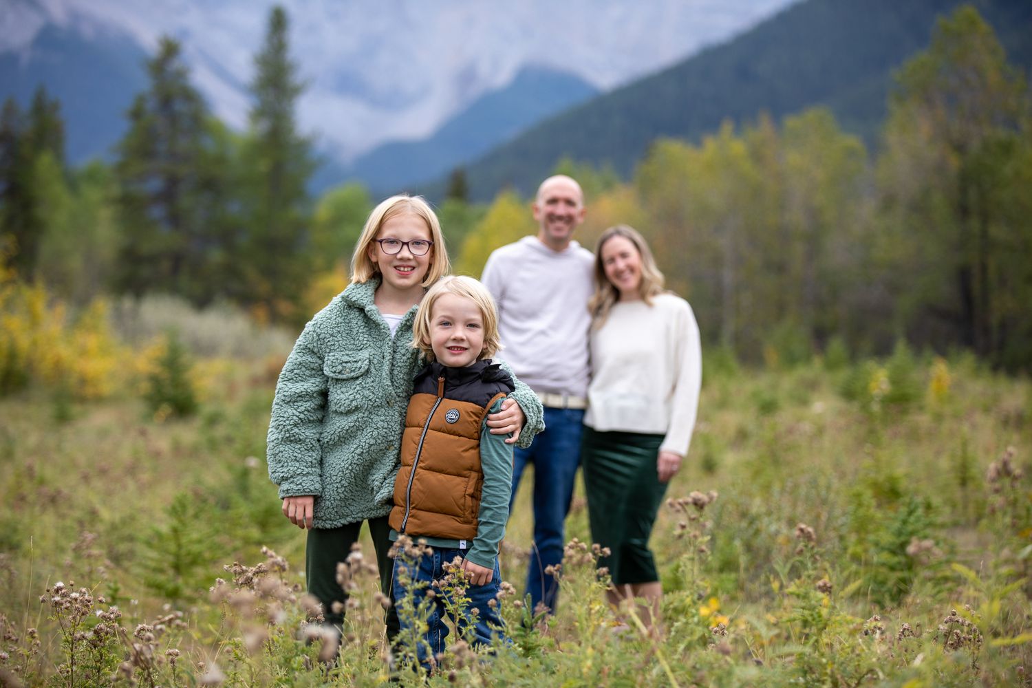 Family enjoying a scenic mountain landscape with evergreen trees and meadows in the background at Quarry Lake Park, Canmore, AB.
