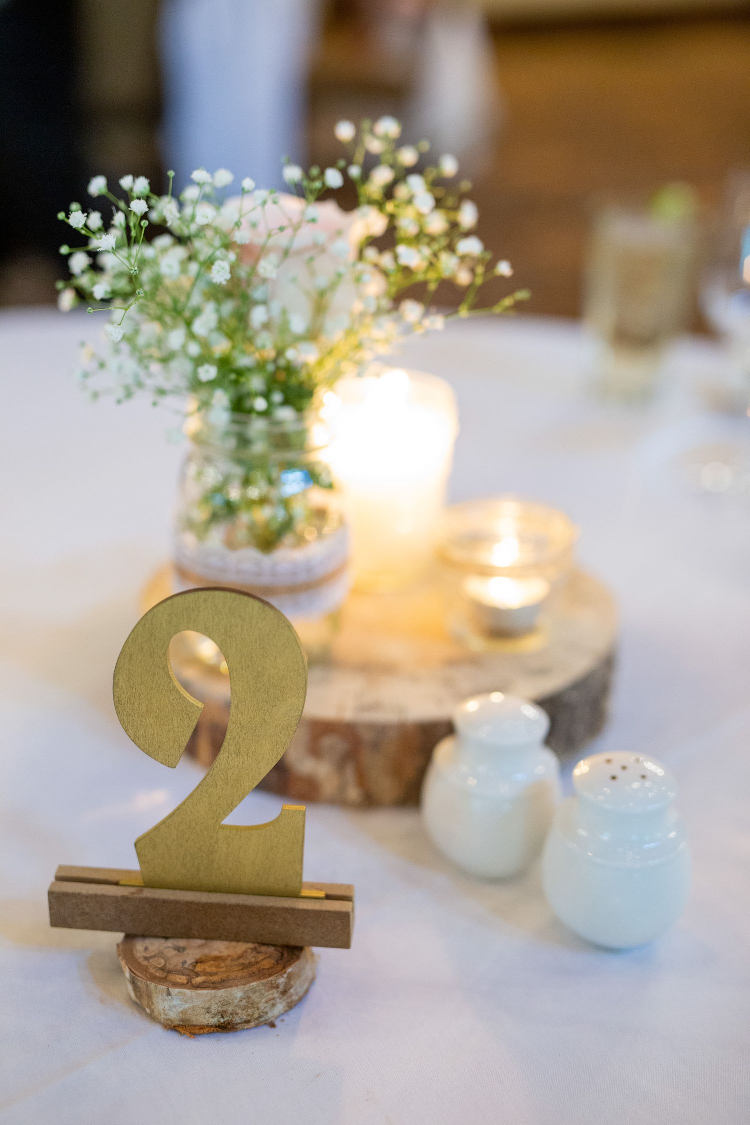 Gold number 2 table marker beside candles and baby's breath flowers on a rustic wood slice wedding centerpiece Silvertip Resort.