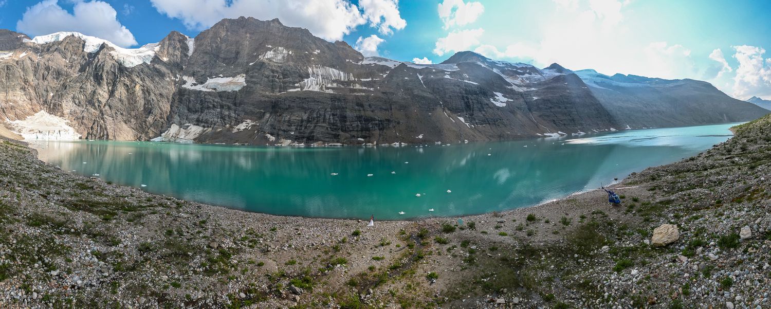 Panoramic view of a turquoise alpine lake surrounded by rocky mountains and glaciers under a partly cloudy sky Lake-of-Hanging-Glacier