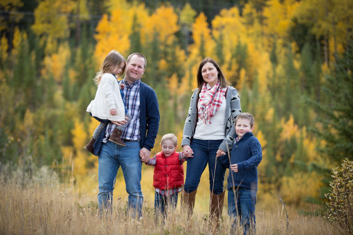 A family walks together through a scenic autumn forest with golden aspen trees in the background at Quarry Lake Park, Canmore, AB.